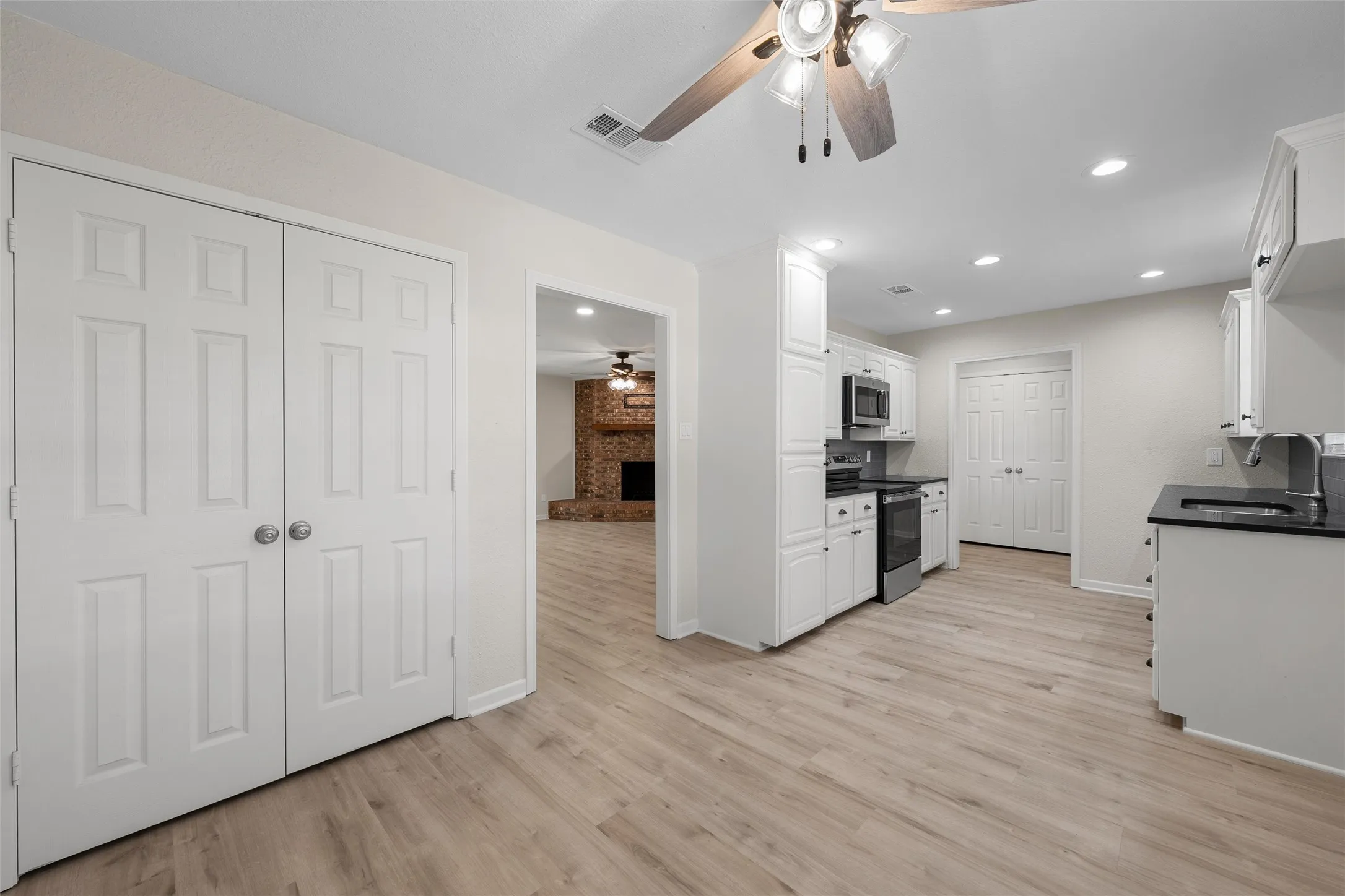 Kitchen with wood-finish flooring, white cabinetry, dark countertops, and recessed lighting