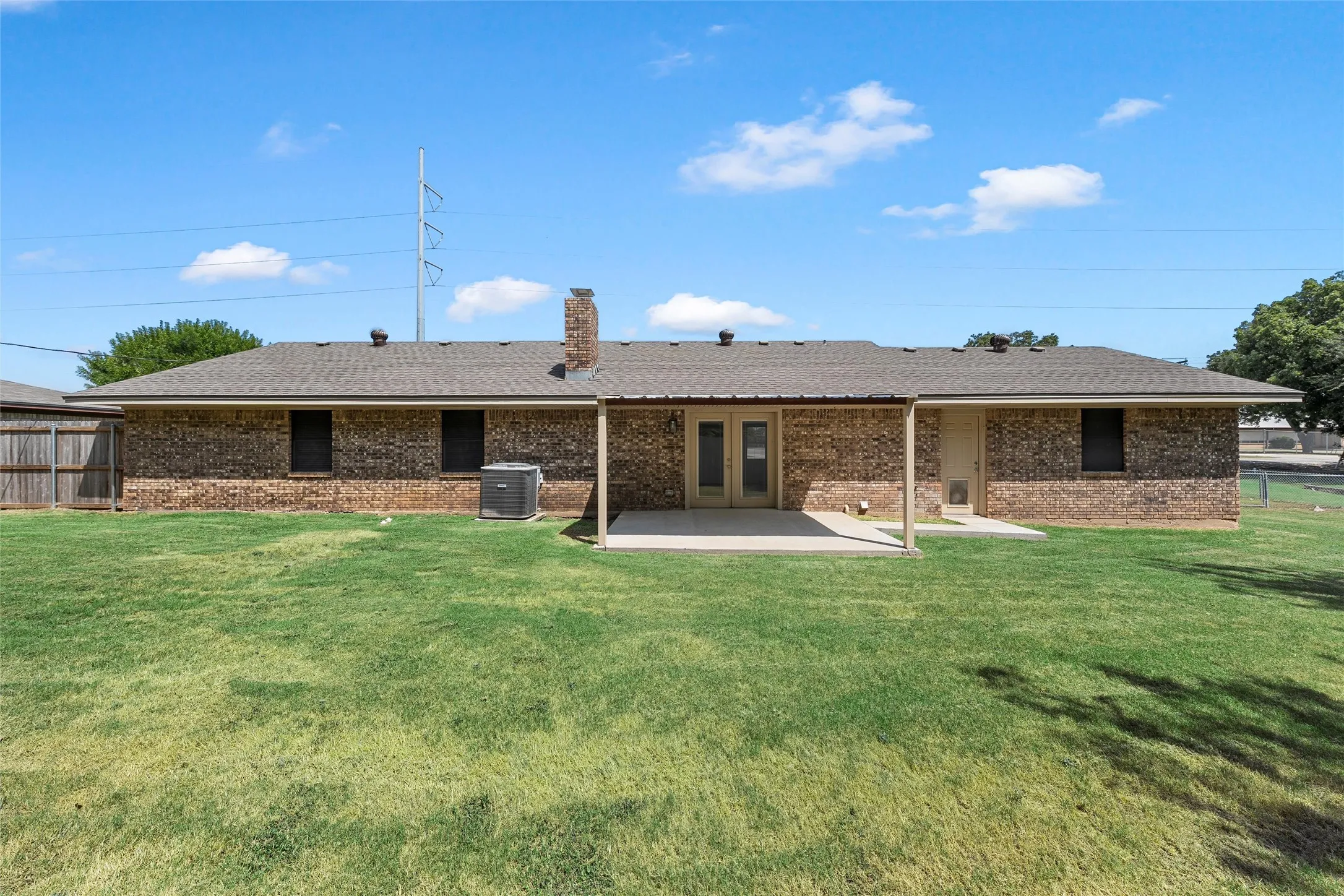 Spacious backyard with a brick exterior, covered patio, and mature landscaping