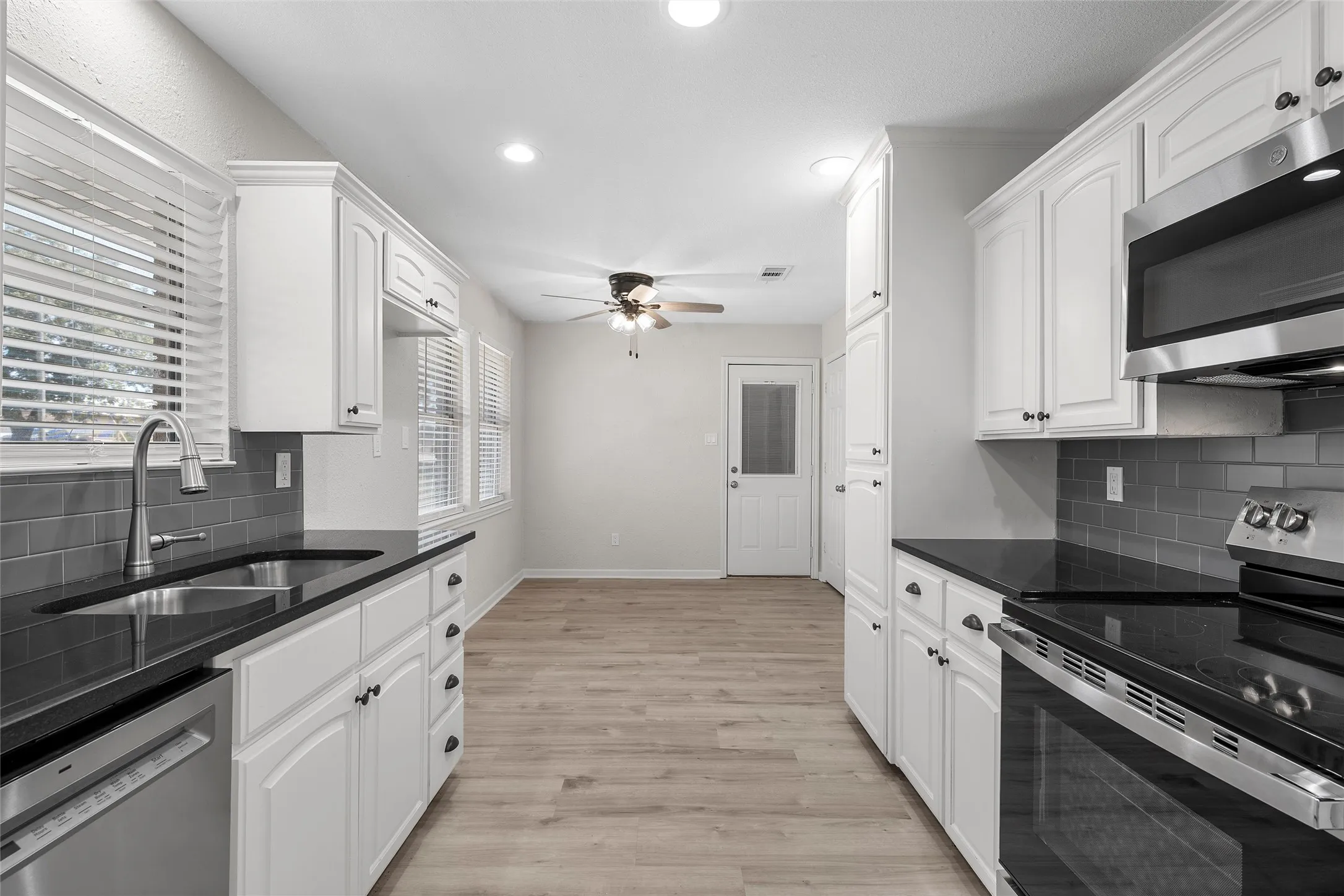 Kitchen featuring white cabinetry, dark countertops, stainless steel appliances, a subway tile backsplash, and light wood-finish flooring