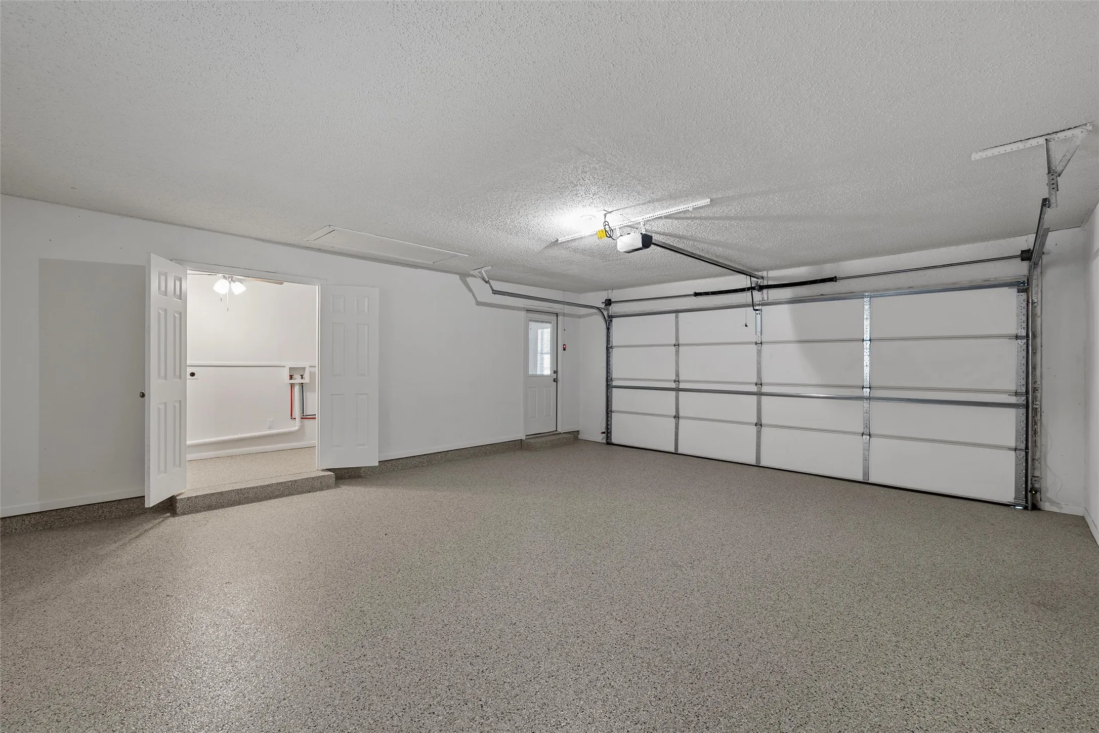 Spacious two-car garage featuring a speckled epoxy floor, white paneled garage door, and a built-in utility area with double doors