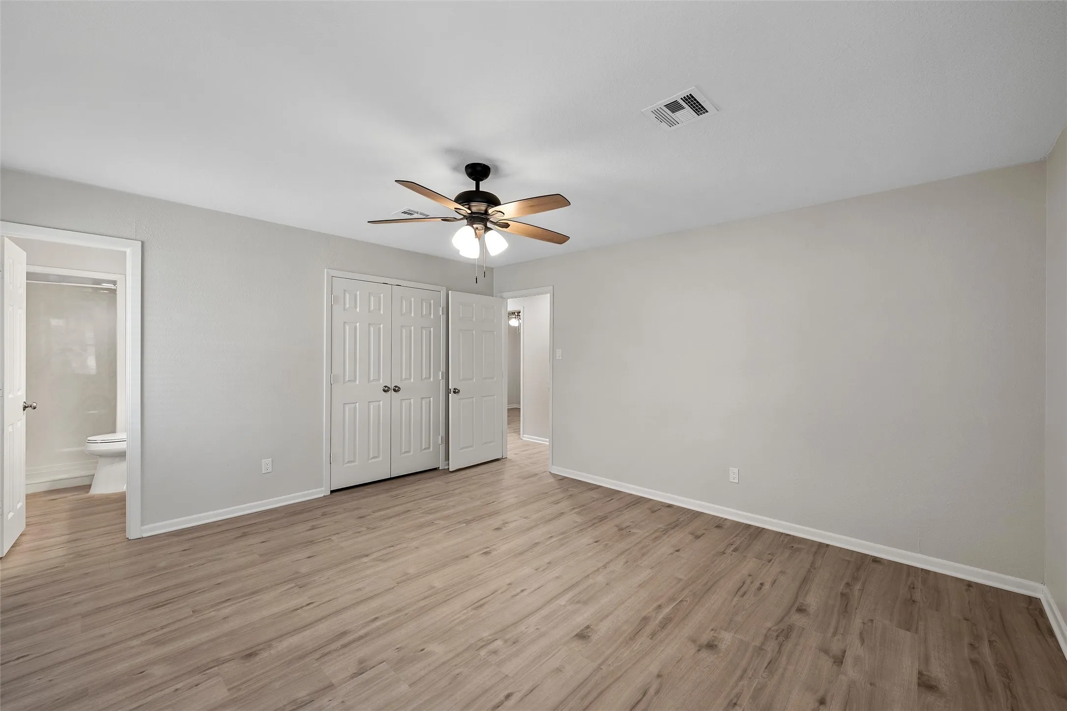 Spacious room featuring wood-finish flooring, a ceiling fan with integrated lighting, and neutral wall tones