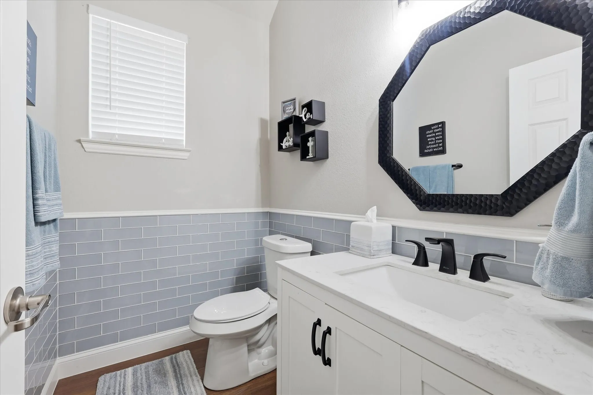White vanity with integrated sink, black fixtures, and a textured octagonal mirror