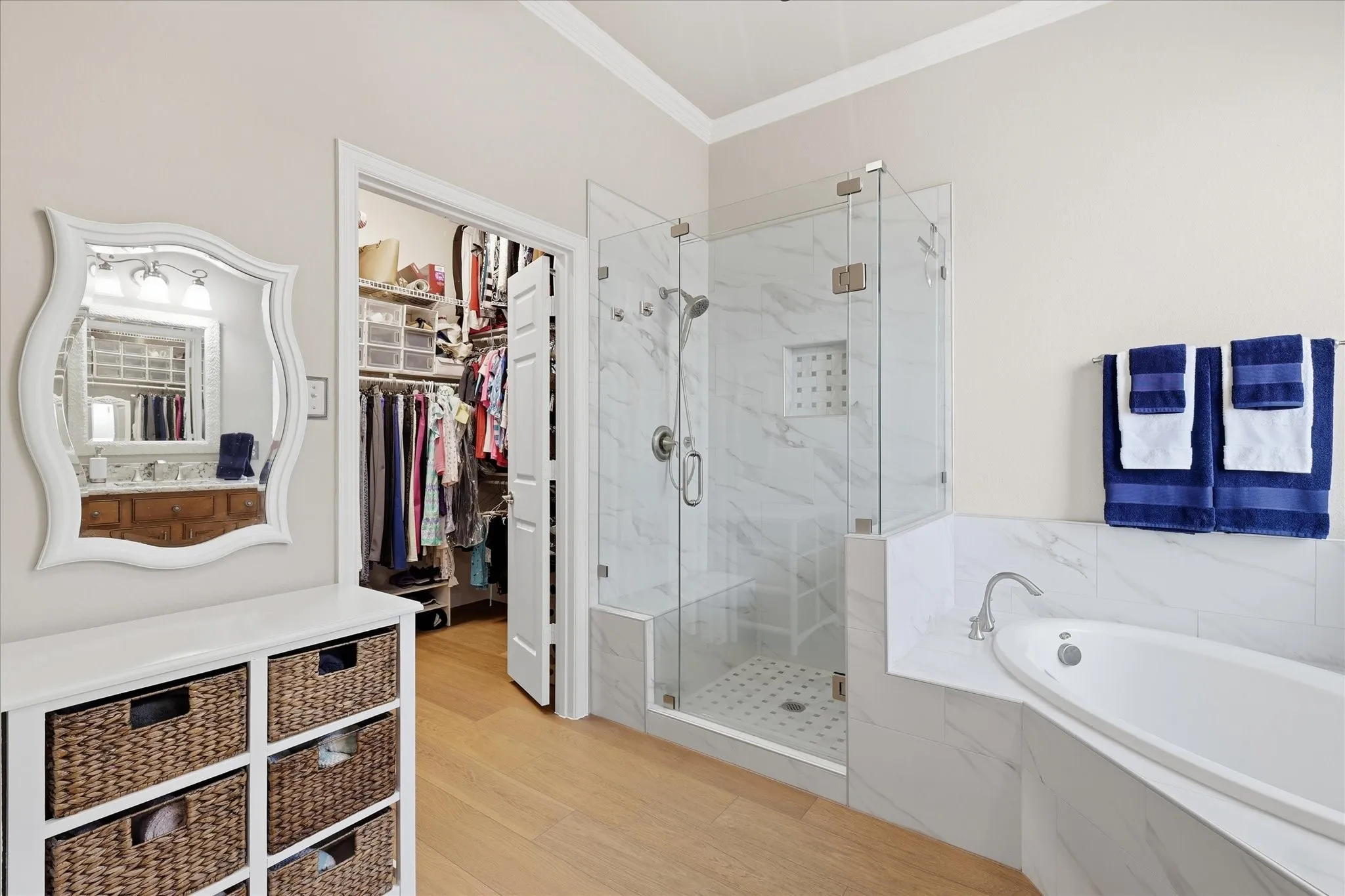 Glass-enclosed shower with a built-in bench, corner soaking tub, and walk-in closet