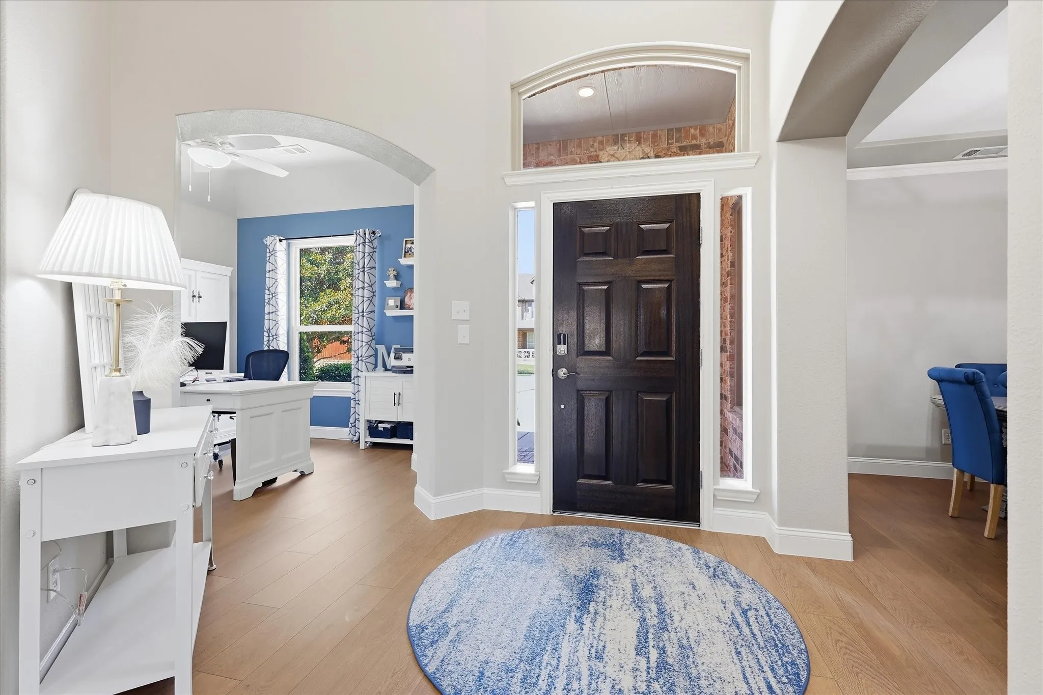Arched entryway with wood-finish flooring, a dark paneled door, and transom window