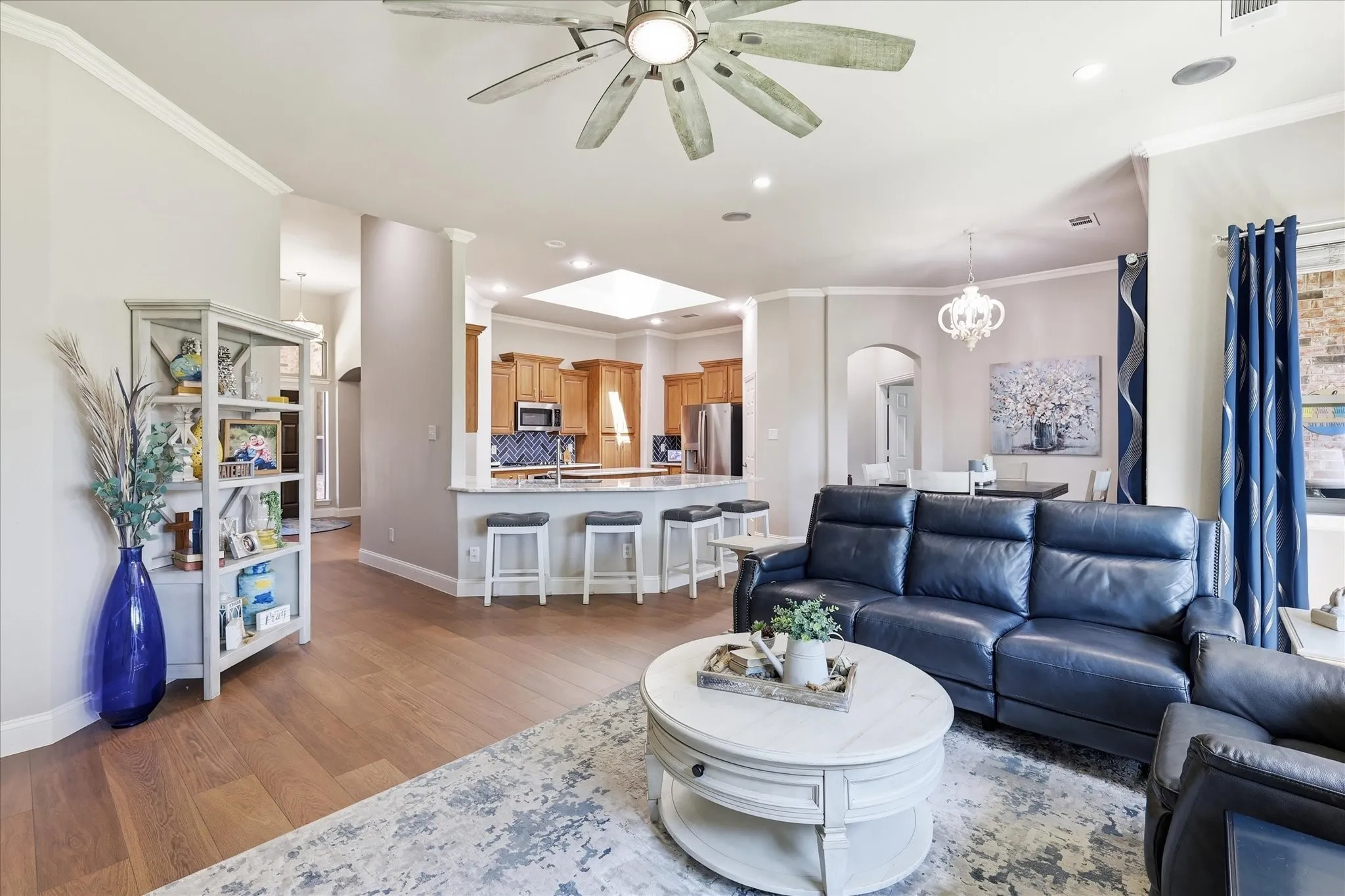 Open-concept living area with wood-finish flooring, a ceiling fan, crown molding, and recessed lighting
