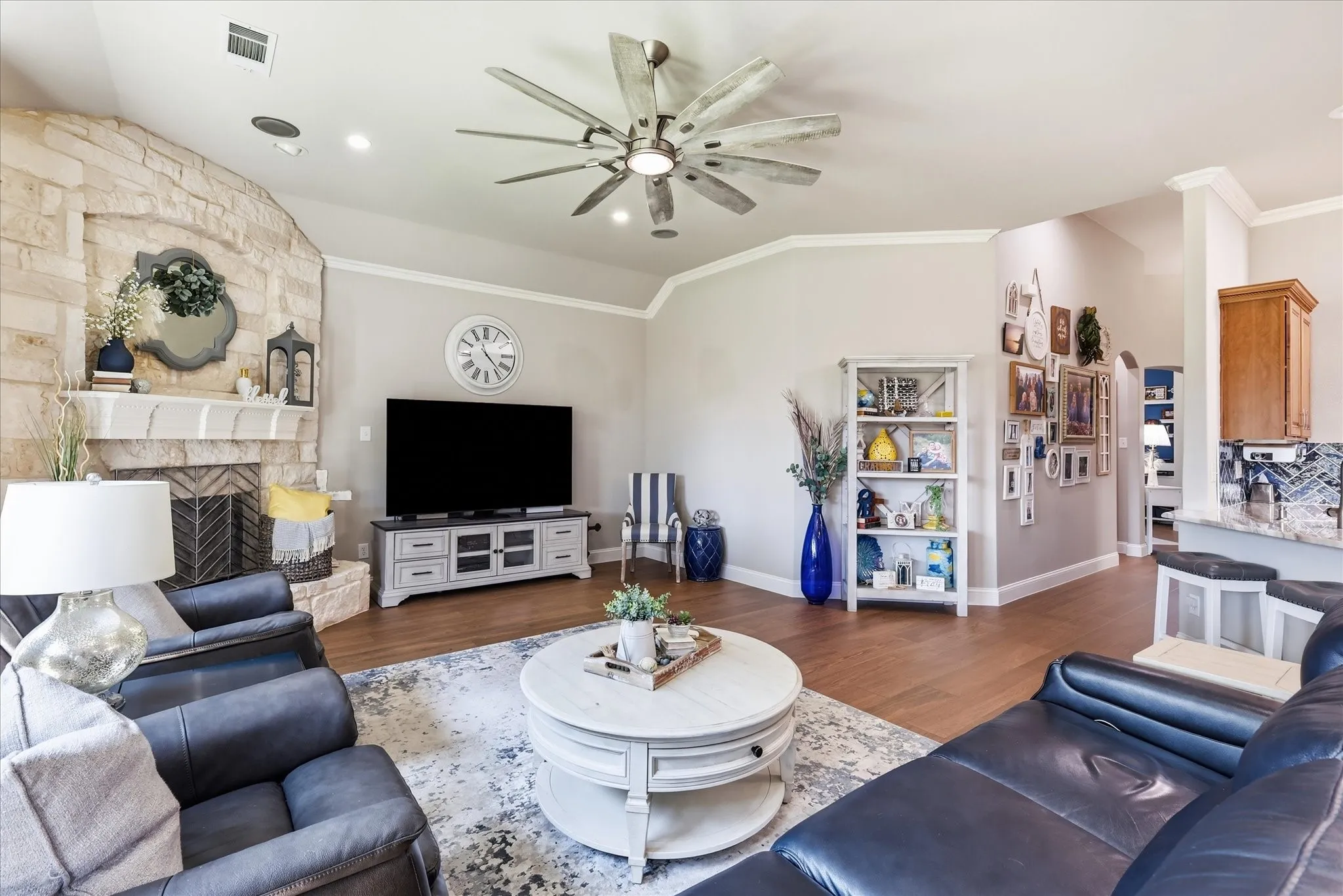 Living area featuring a stone-clad fireplace with mantel, crown molding, wood-finish flooring, recessed lighting, and a multi-blade ceiling​​‌​​​​‌​​‌‌​‌‌​​​‌‌​‌​‌​‌​​​‌​​ fan