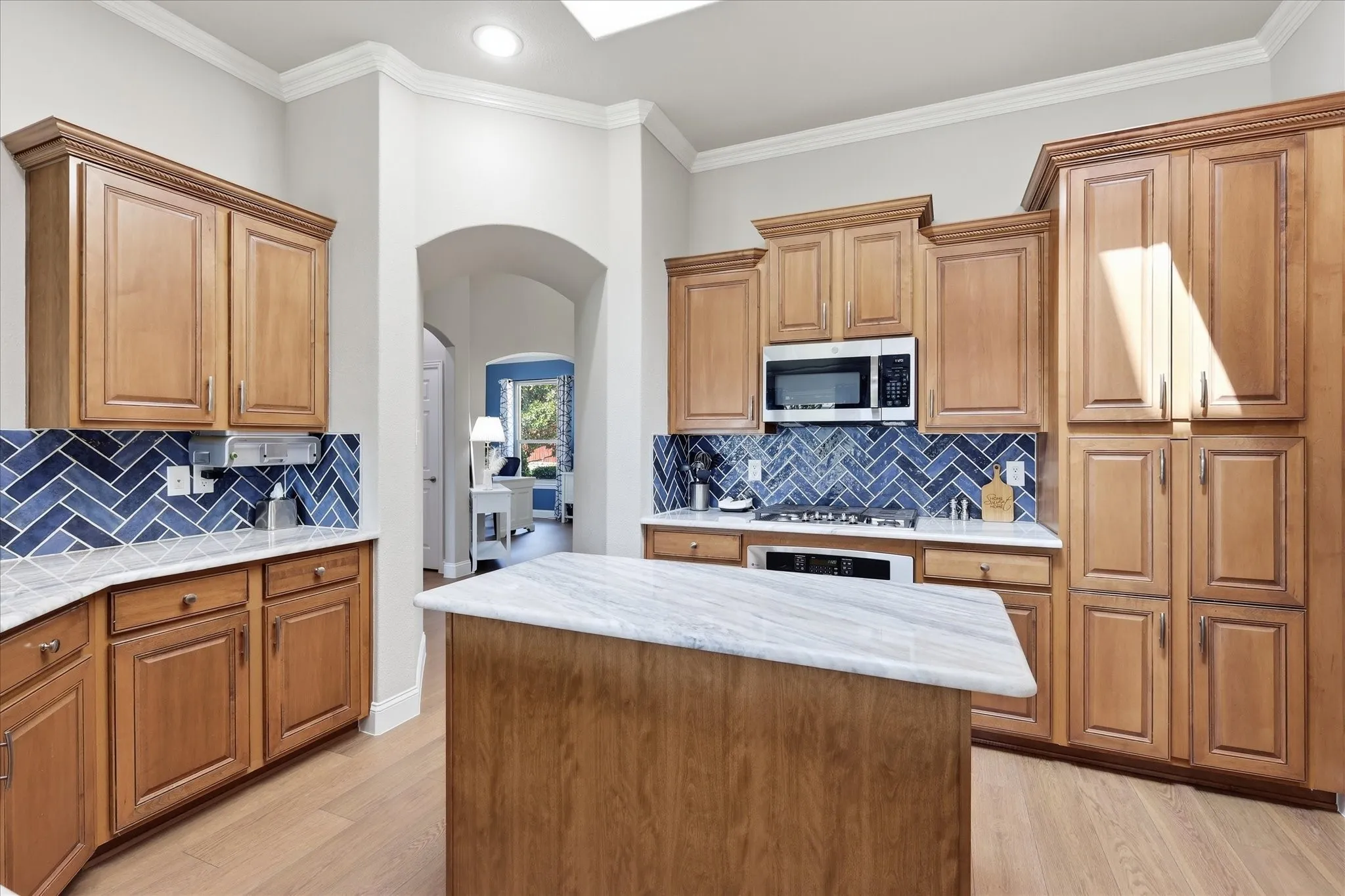 Kitchen featuring wood cabinetry, herringbone tile backsplash, an island with a light-toned countertop, and recessed lighting