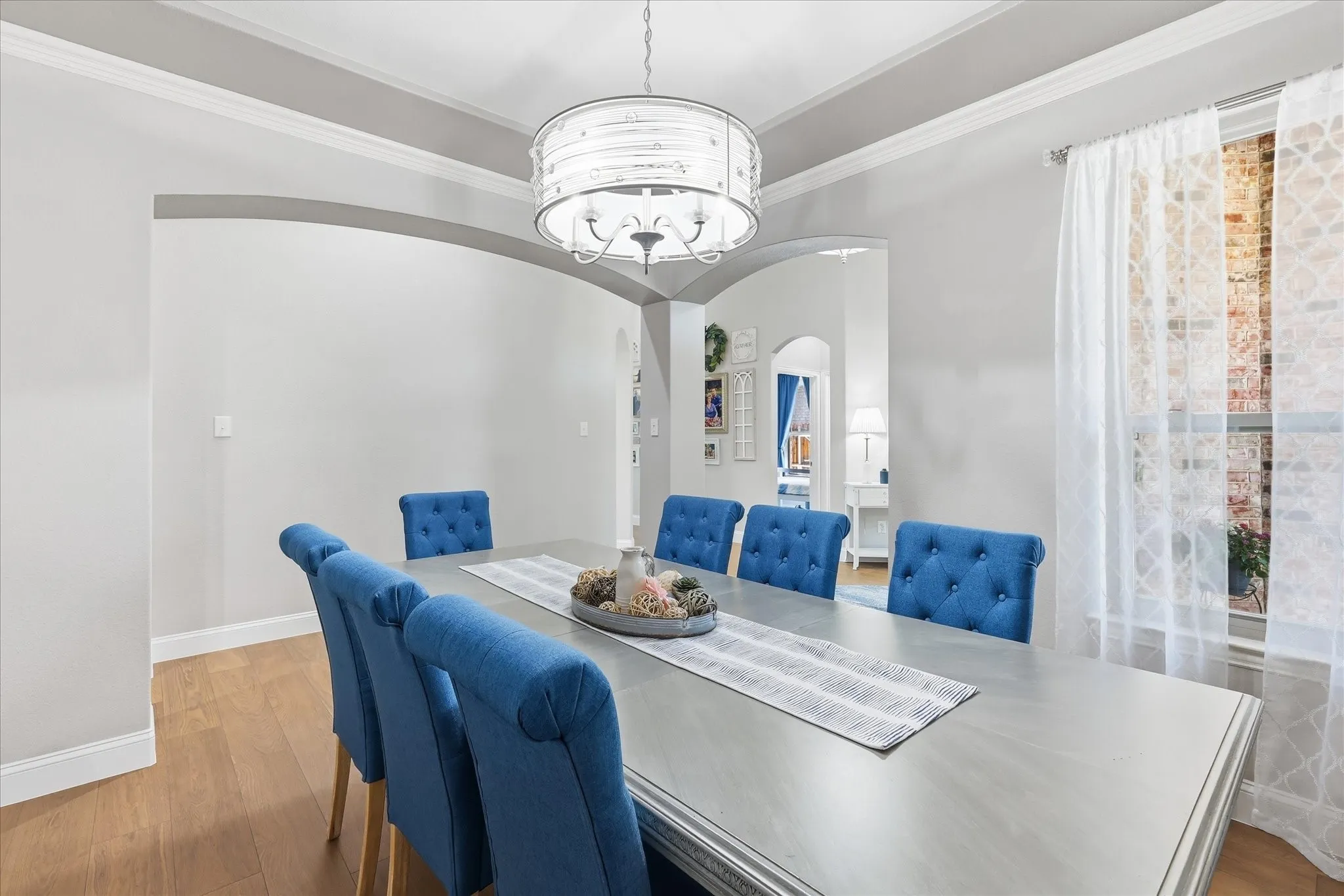 Tray ceiling with crown molding, drum chandelier, archway, wood-finish flooring, and a large window