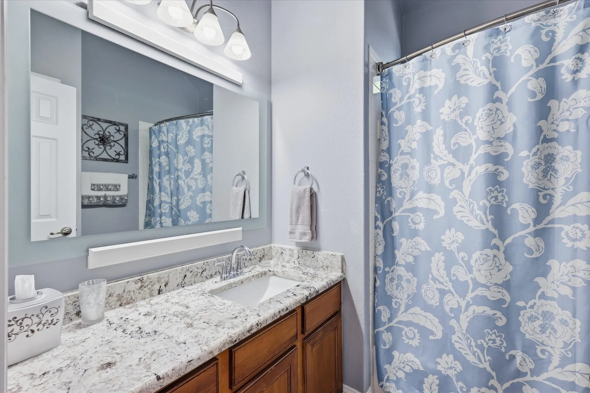 Granite-style countertop with integrated sink, wood-finish vanity cabinetry, and overhead vanity lighting