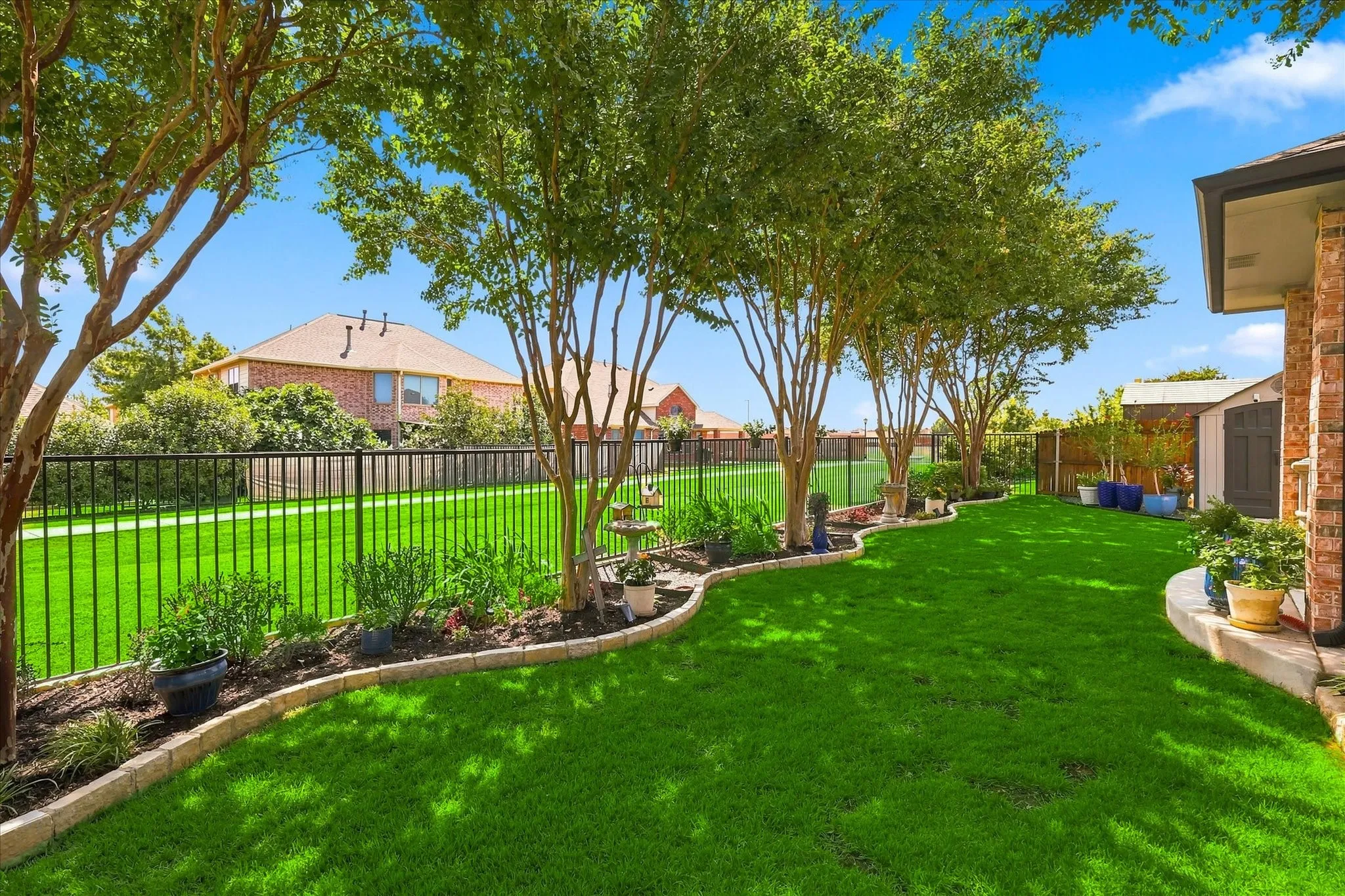Expansive backyard featuring a lush lawn, mature trees, and a black wrought iron fence