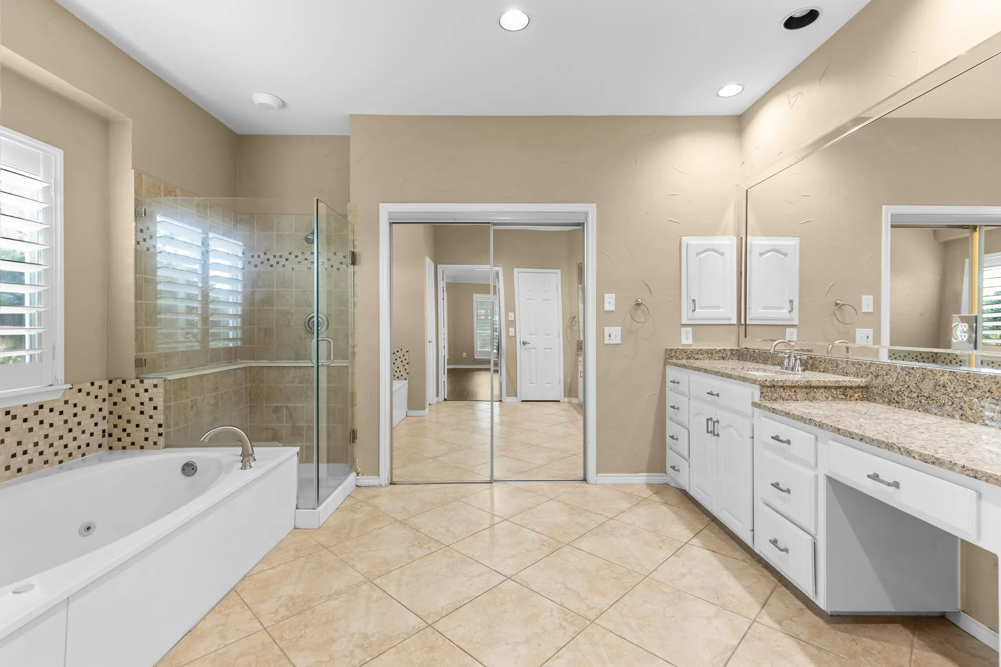 Dual vanity with stone countertops, walk-in shower with glass enclosure, soaking tub, and tile flooring