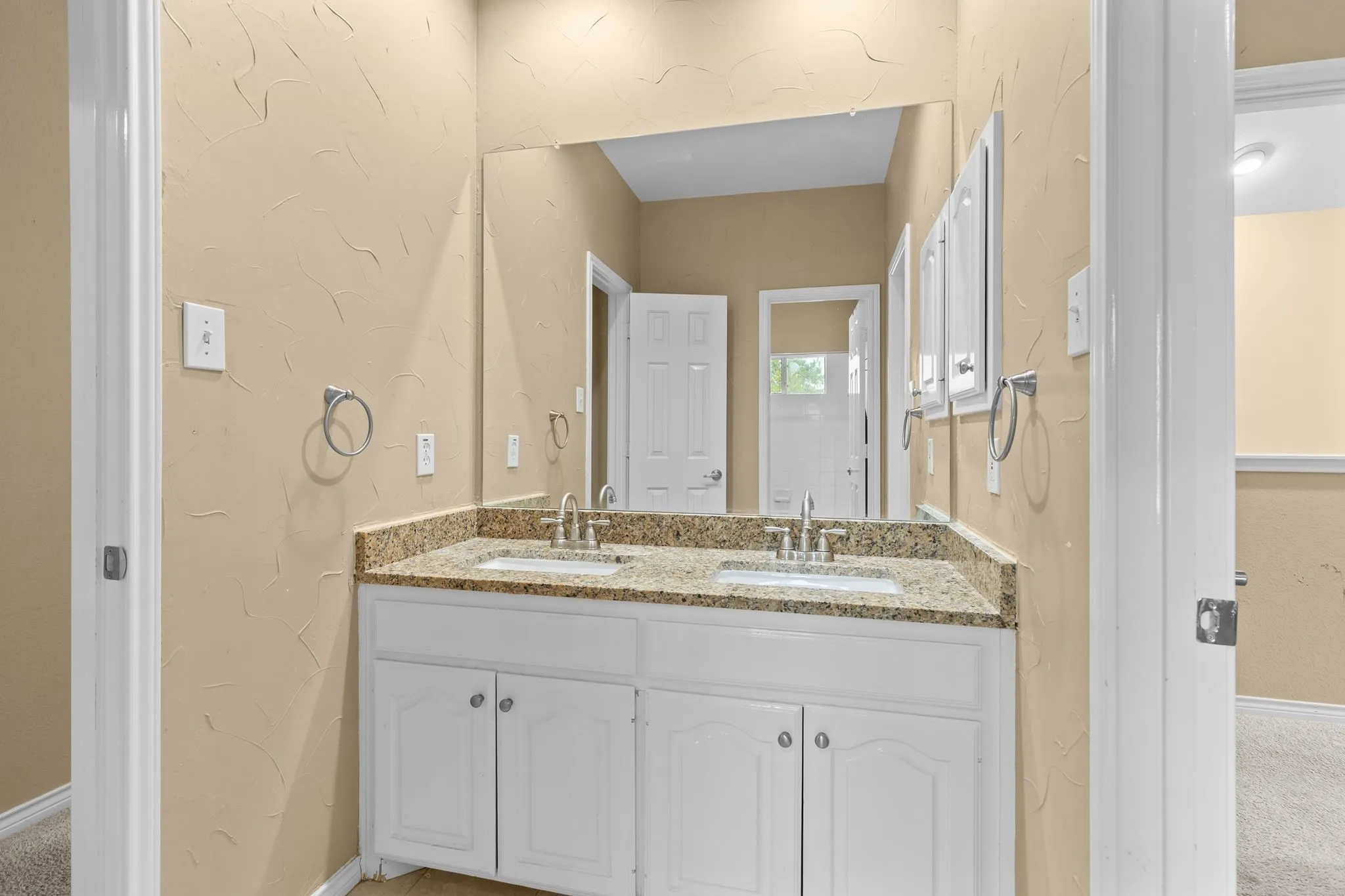 Dual sink vanity with stone-finish countertop, white cabinetry, and wall-mounted mirror