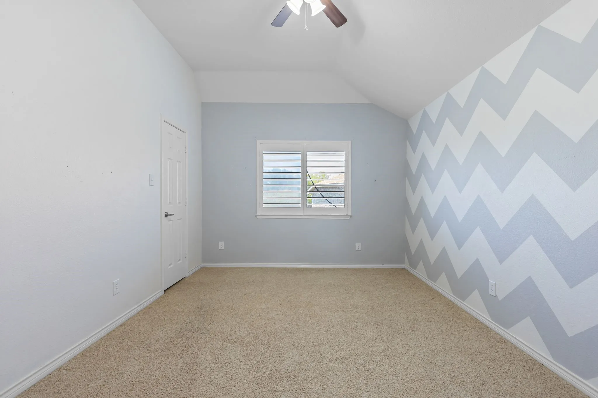Carpeted flooring, window with shutters, white six-panel door, ceiling fan, and chevron accent wall
