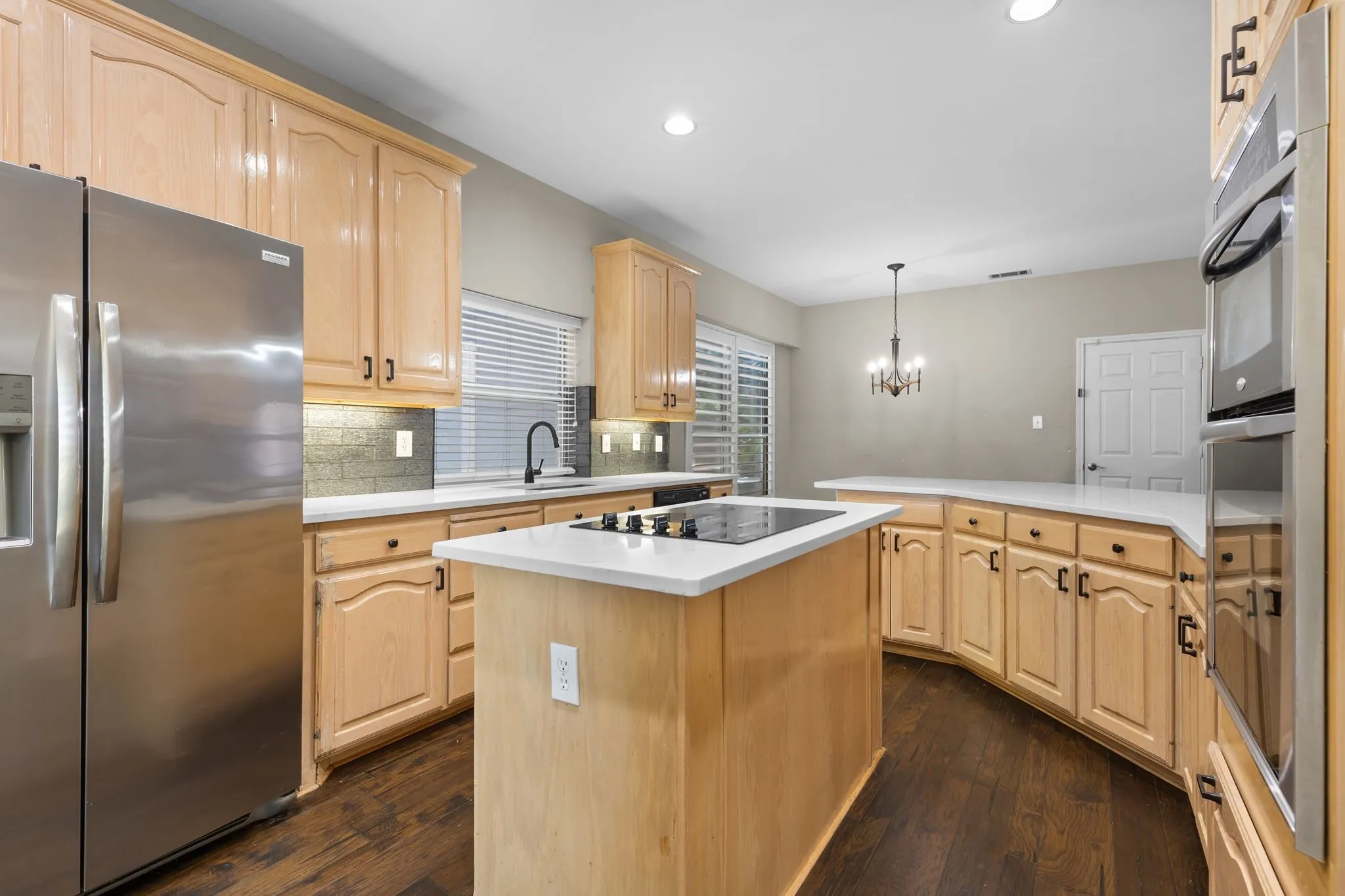 Kitchen featuring wood-finish cabinetry, stainless steel appliances, a center island with cooktop, and light-toned countertops