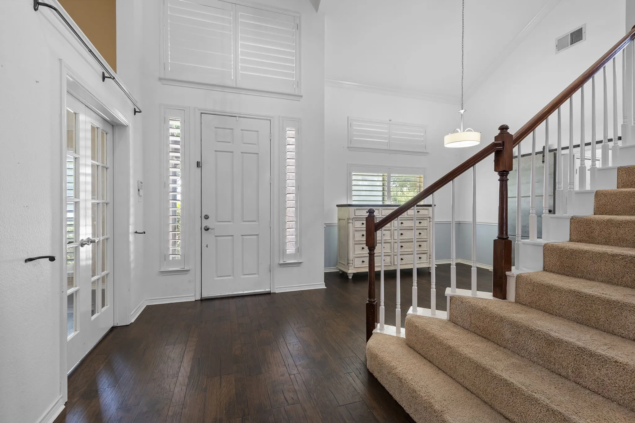 Expansive foyer with vaulted ceilings, wood-finish flooring, a paneled entry door with sidelights, and a carpeted staircase with wood newel posts