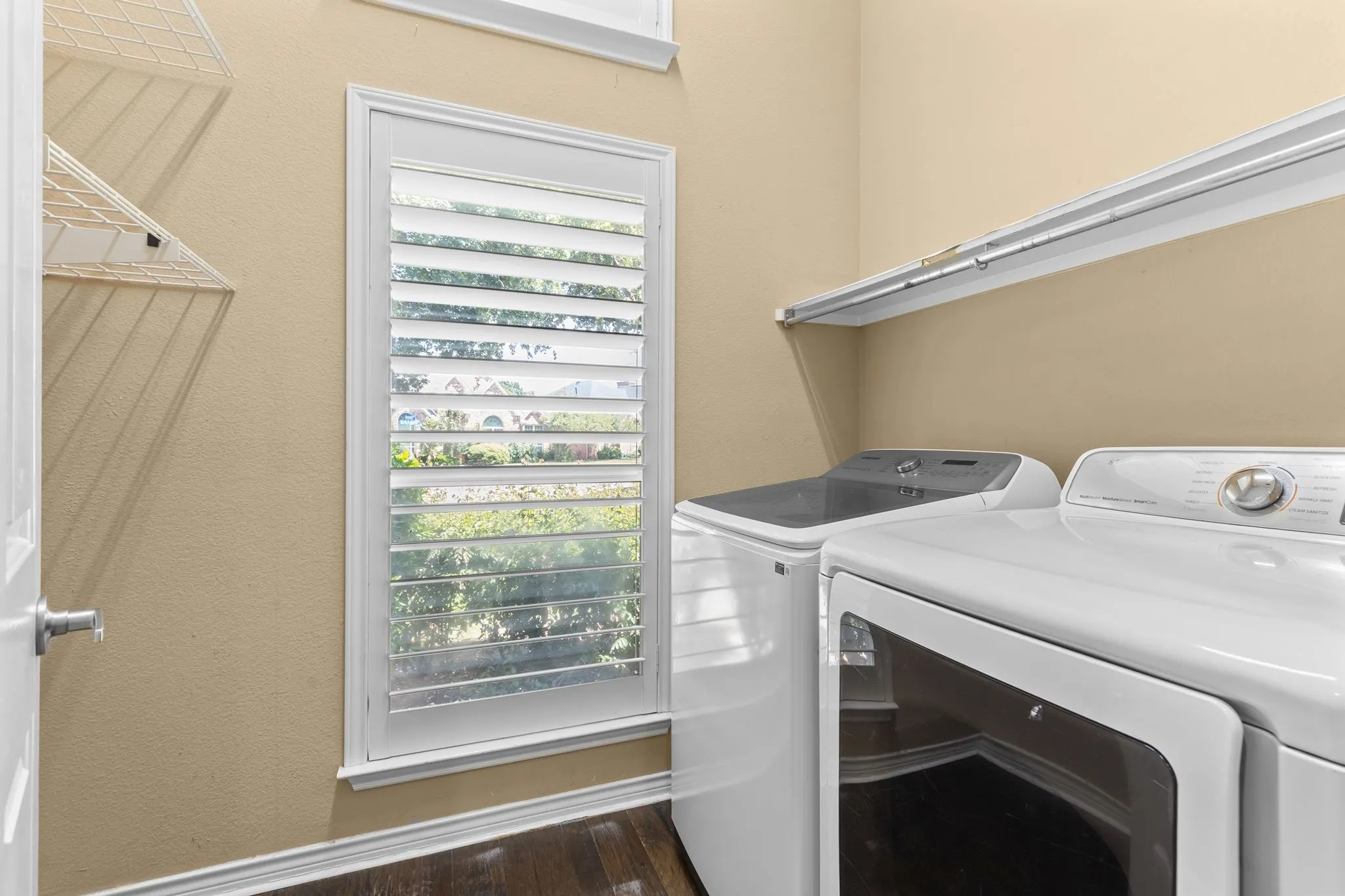 Laundry area with wood-finish flooring, a window featuring plantation shutters, and a wall-mounted shelving unit