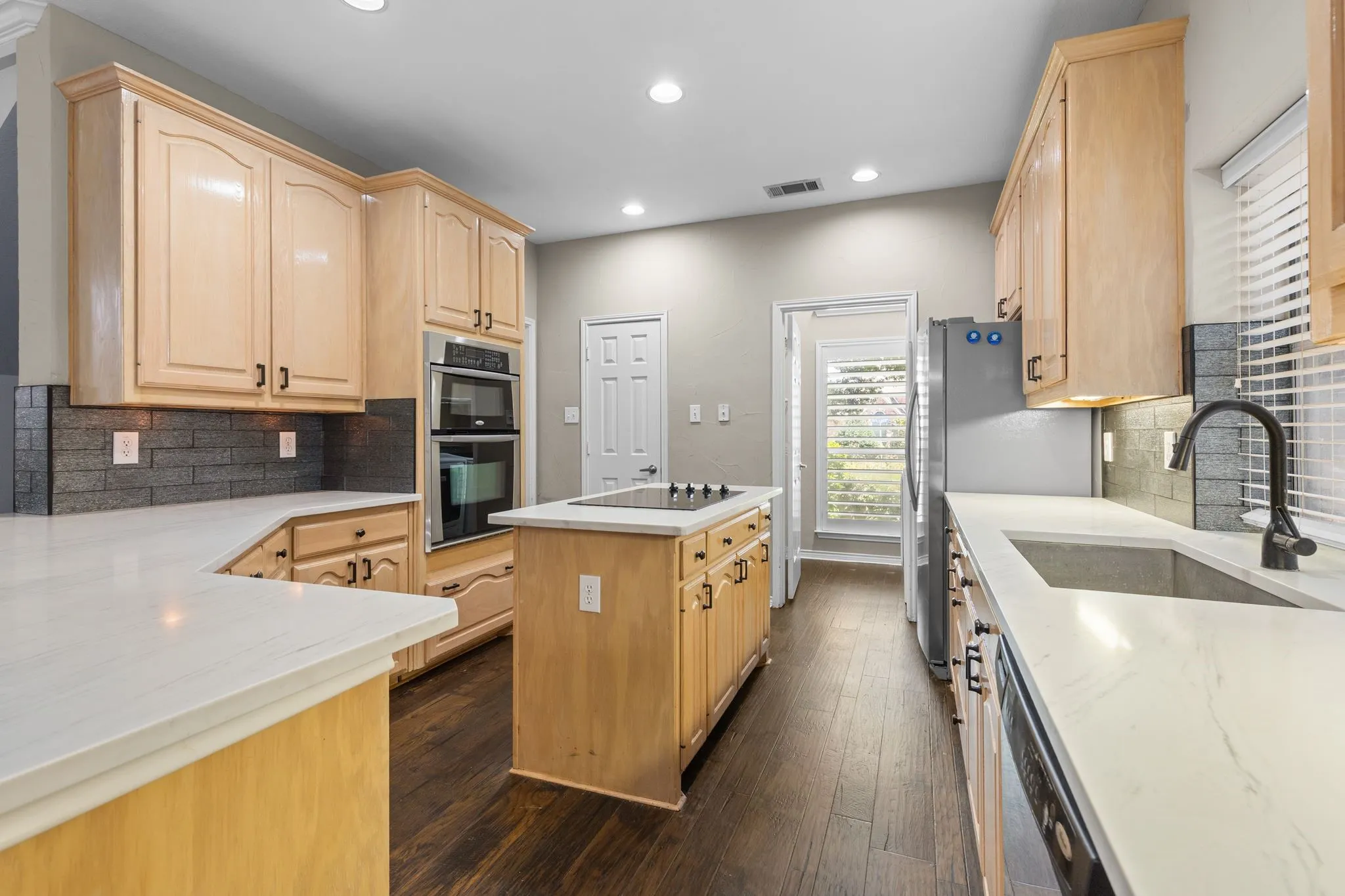Kitchen featuring wood-finish flooring, light-toned cabinetry, white countertops, built-in double ovens, and a center island with a cooktop