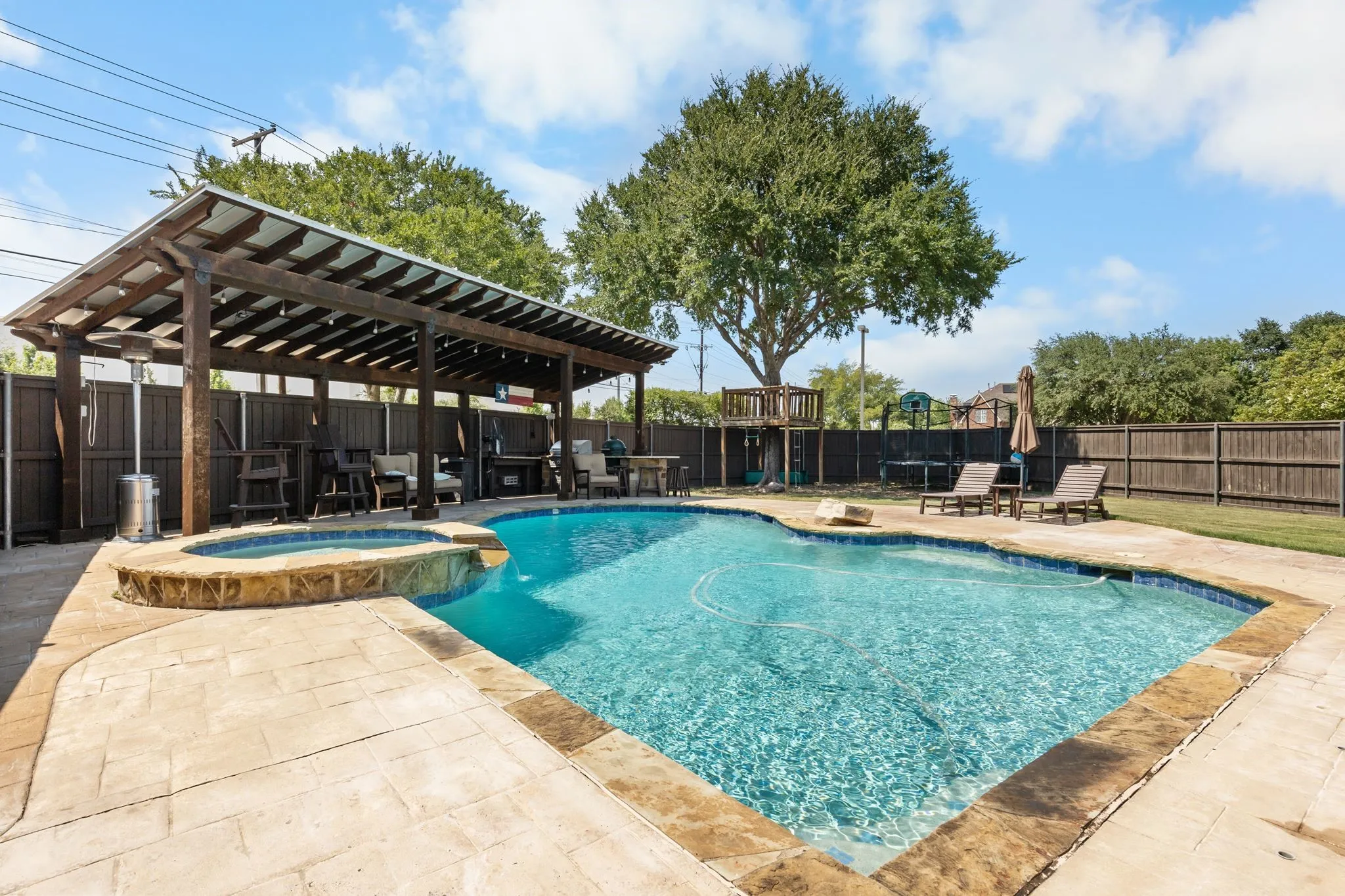 Swimming pool with integrated spa, covered patio with wood beams, concrete stamped patio, and mature trees