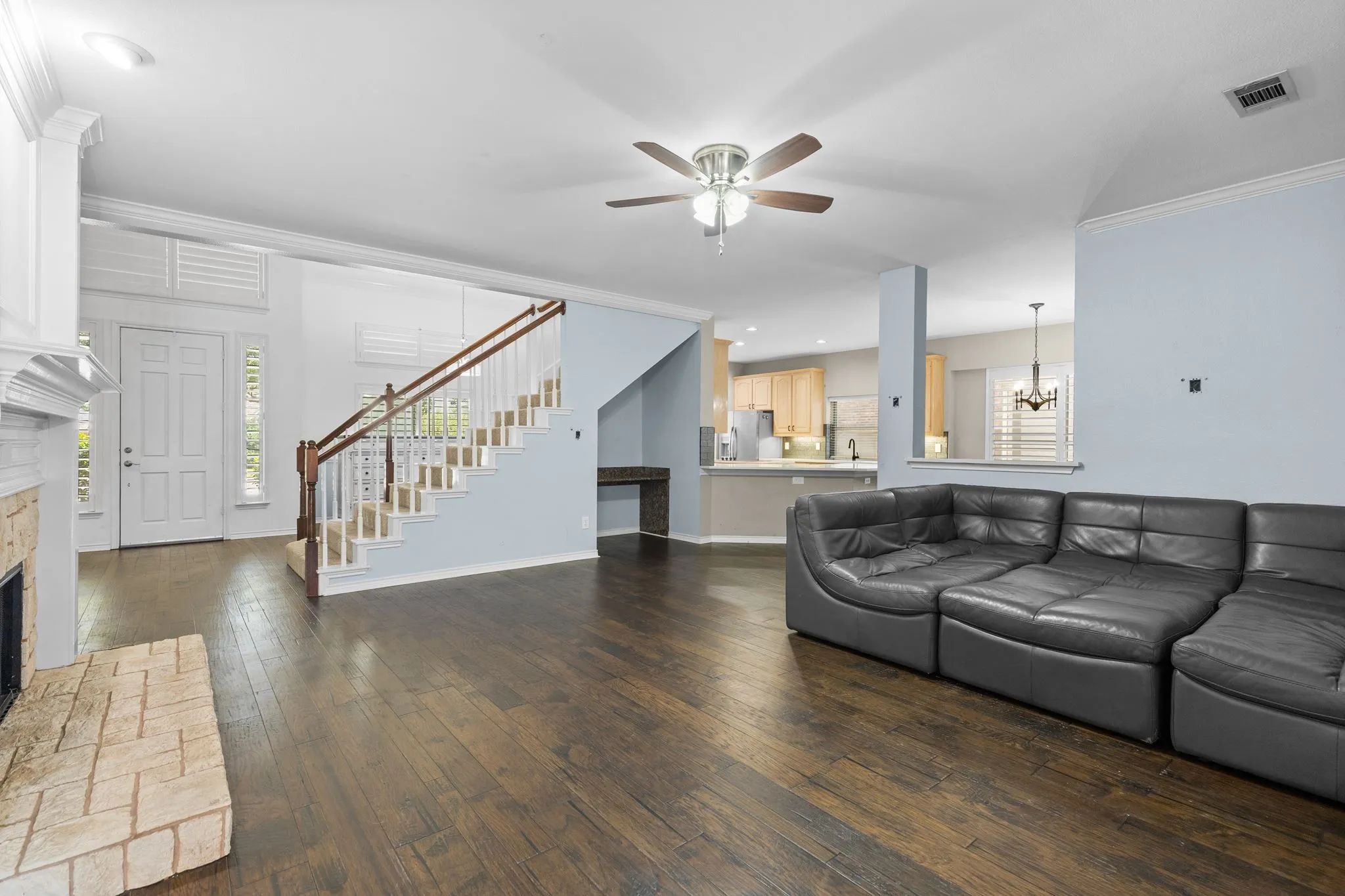 Open-concept living area featuring wood-finish flooring, a fireplace with a stone surround, and a staircase with wood handrails
