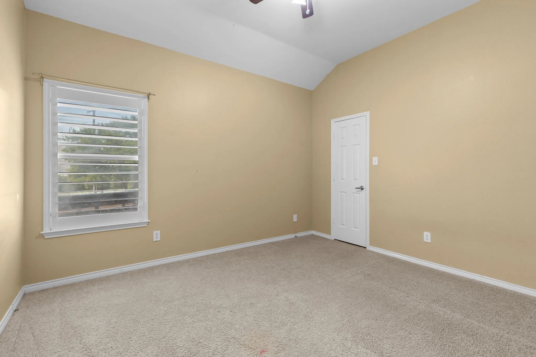 Vaulted ceiling with an attached ceiling fan, neutral carpet flooring, and a window with plantation shutters