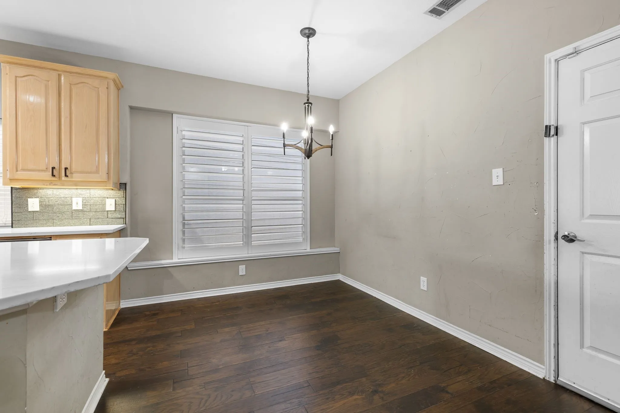 Hardwood-style flooring, white window shutters, a contemporary chandelier, light-toned walls, and white trim