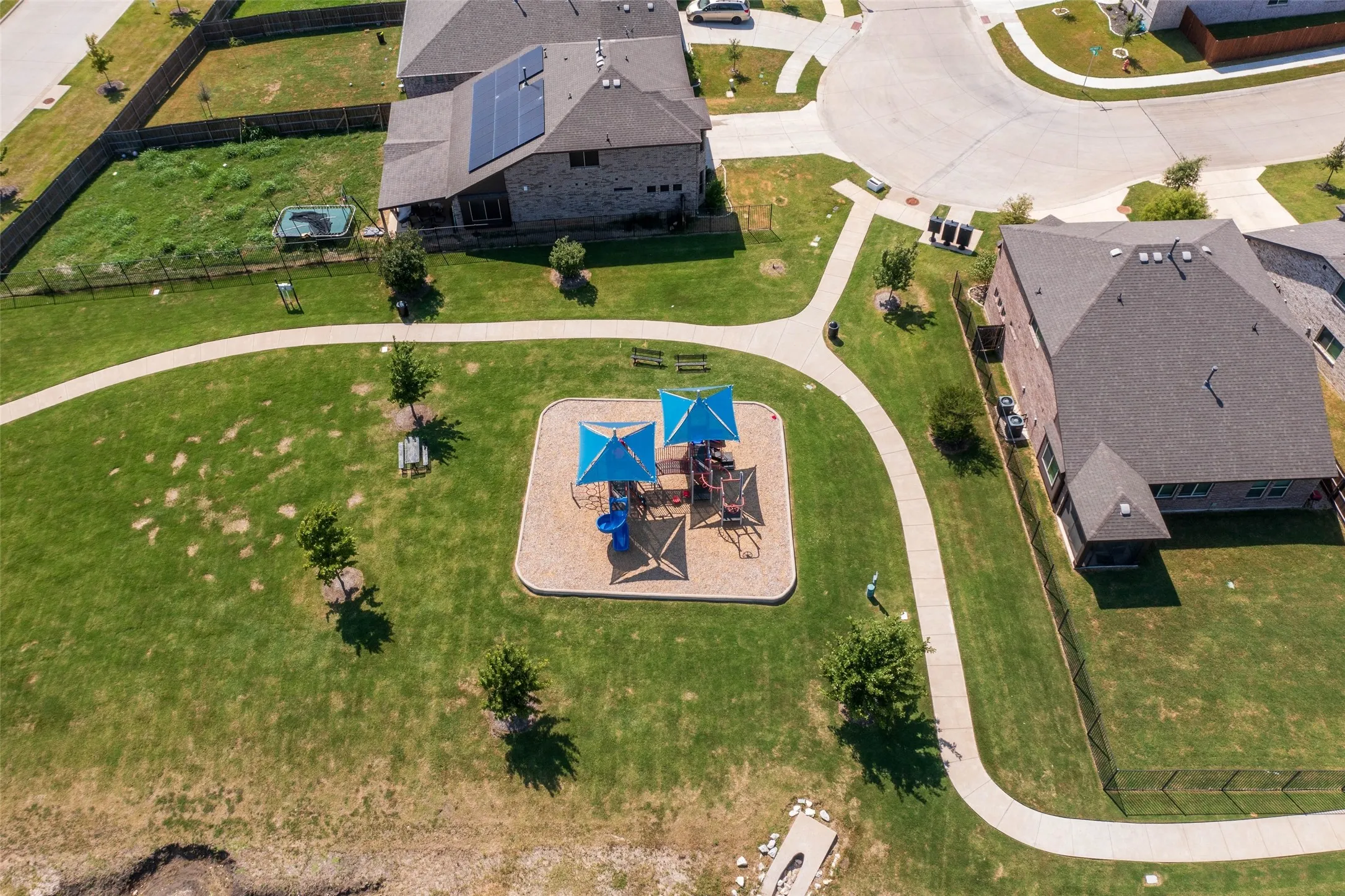 Community park featuring a playground with blue shade canopies, a paved walking path, and open green space