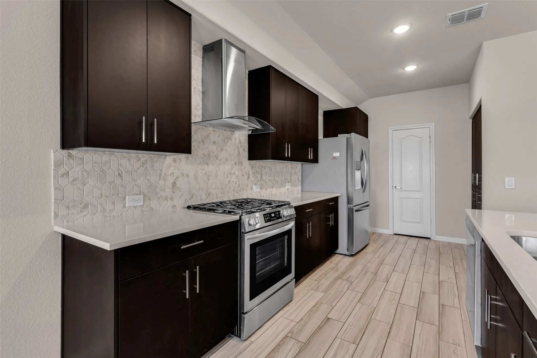 Modern kitchen featuring dark wood-finish cabinetry, light stone countertops, and a full stainless steel appliance package including a range with hood and refrigerator