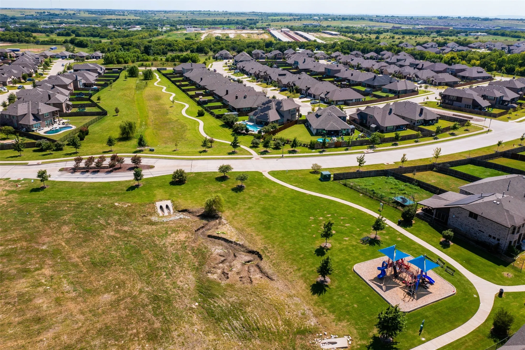 Community green space featuring a playground with shade canopies, paved walking paths, and manicured lawns