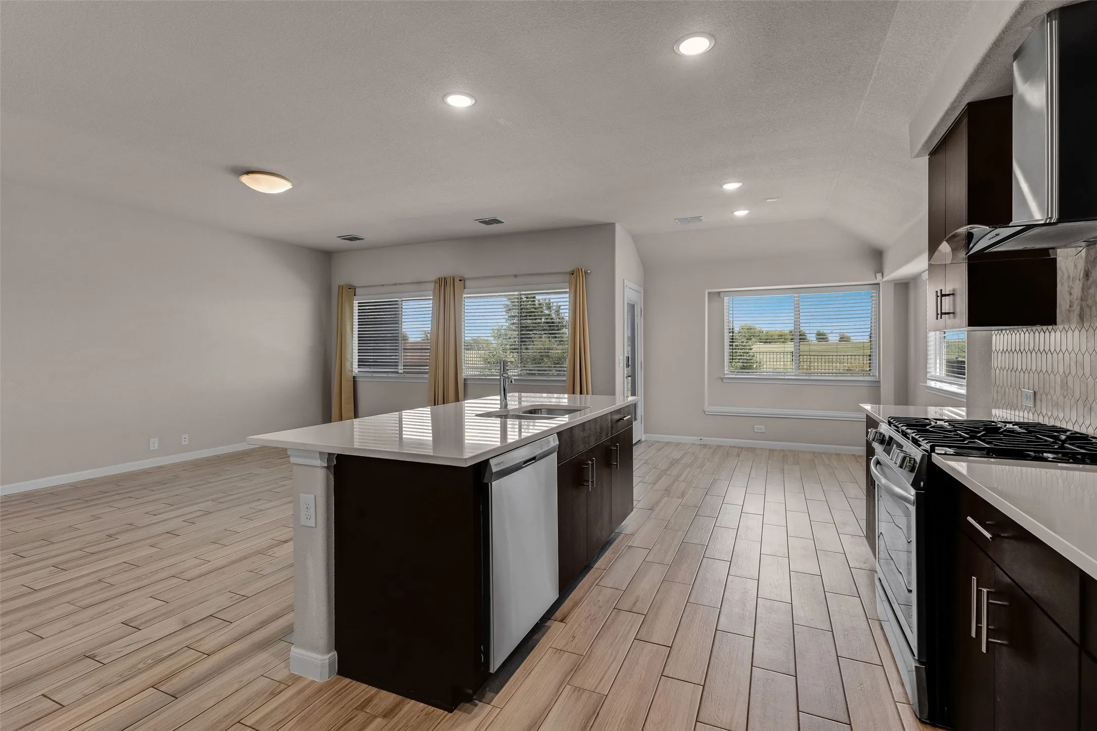 Open concept kitchen featuring dark wood cabinetry, light-toned countertops, and a full suite of stainless steel appliances