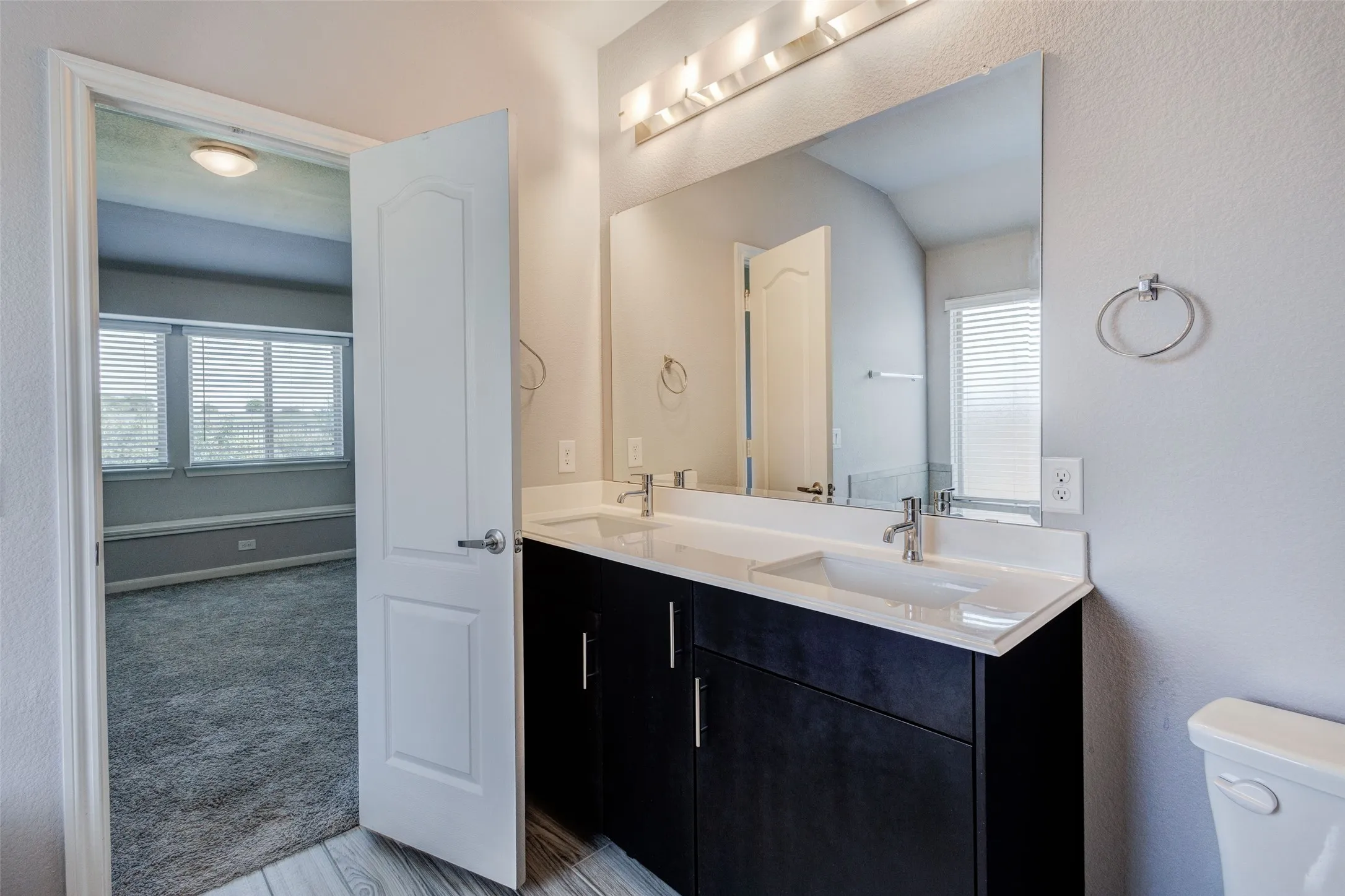Bathroom featuring a dual vanity with undermount sinks and dark cabinetry, a large mirror, and wall-mounted light fixture