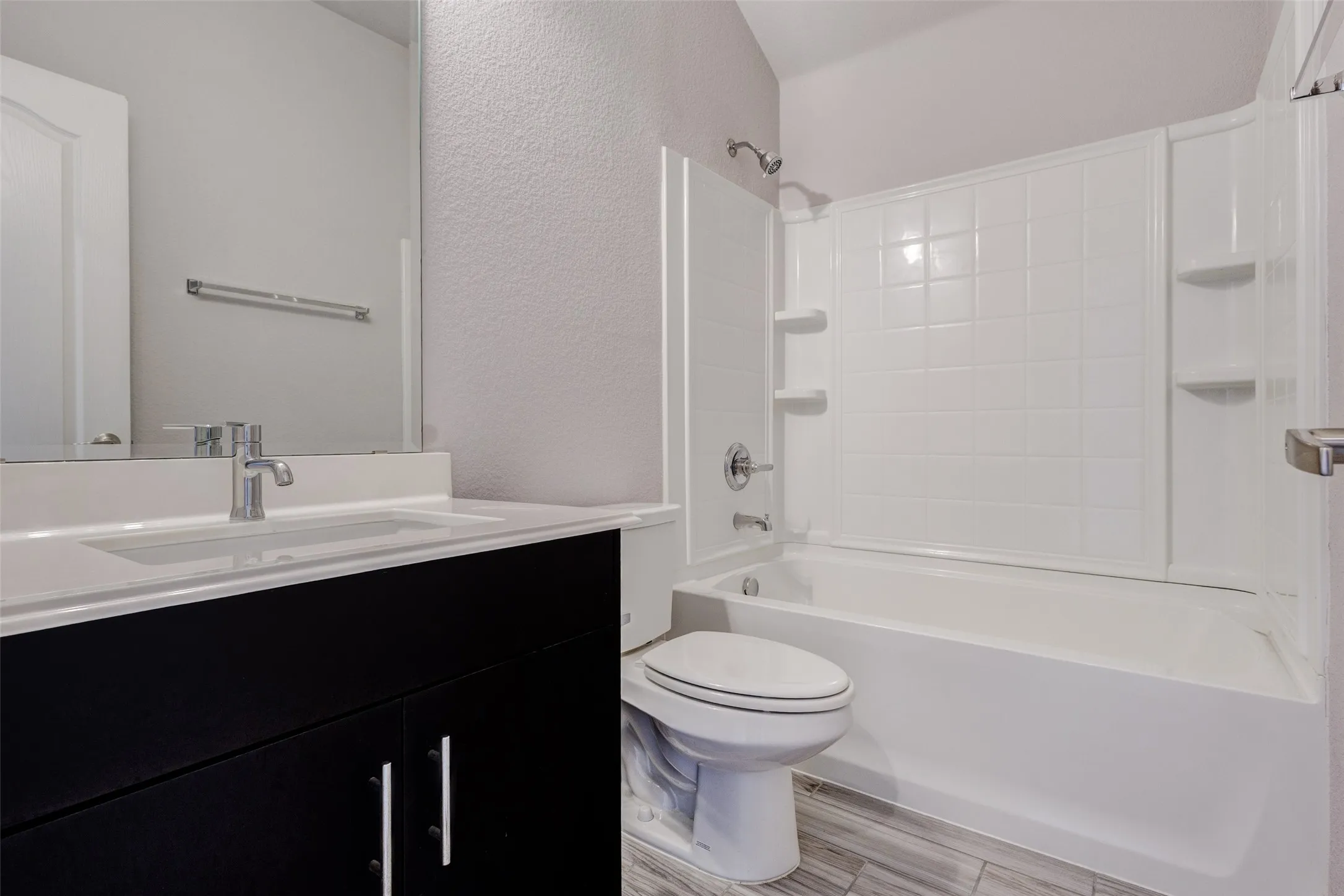 Bathroom featuring a white bathtub with a tiled shower surround, a white toilet, and a vanity with a white countertop and a dark wood-finish cabinet
