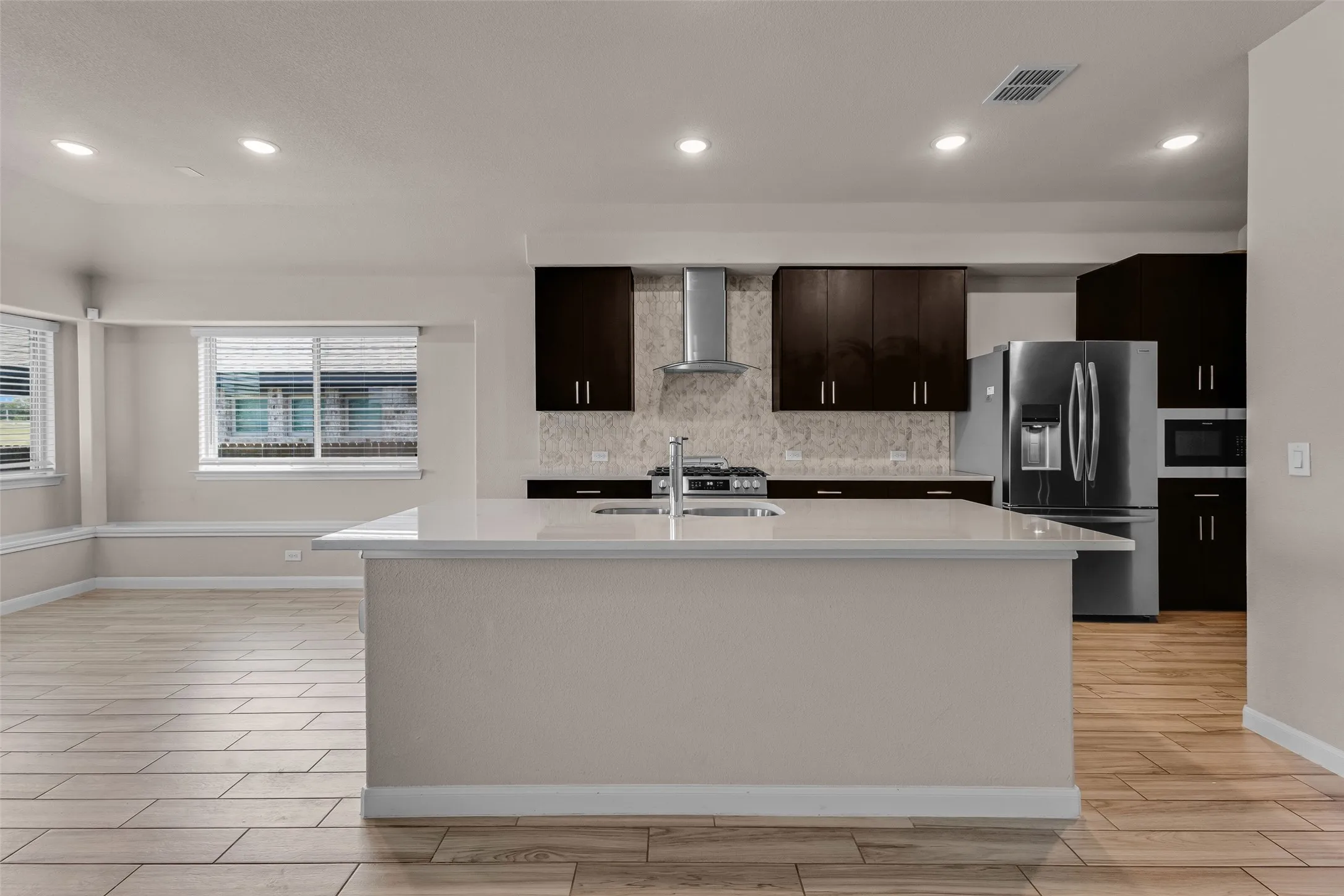 Kitchen featuring an island with a built-in sink, dark wood-finish cabinetry, stainless steel appliances, and wood-finish flooring