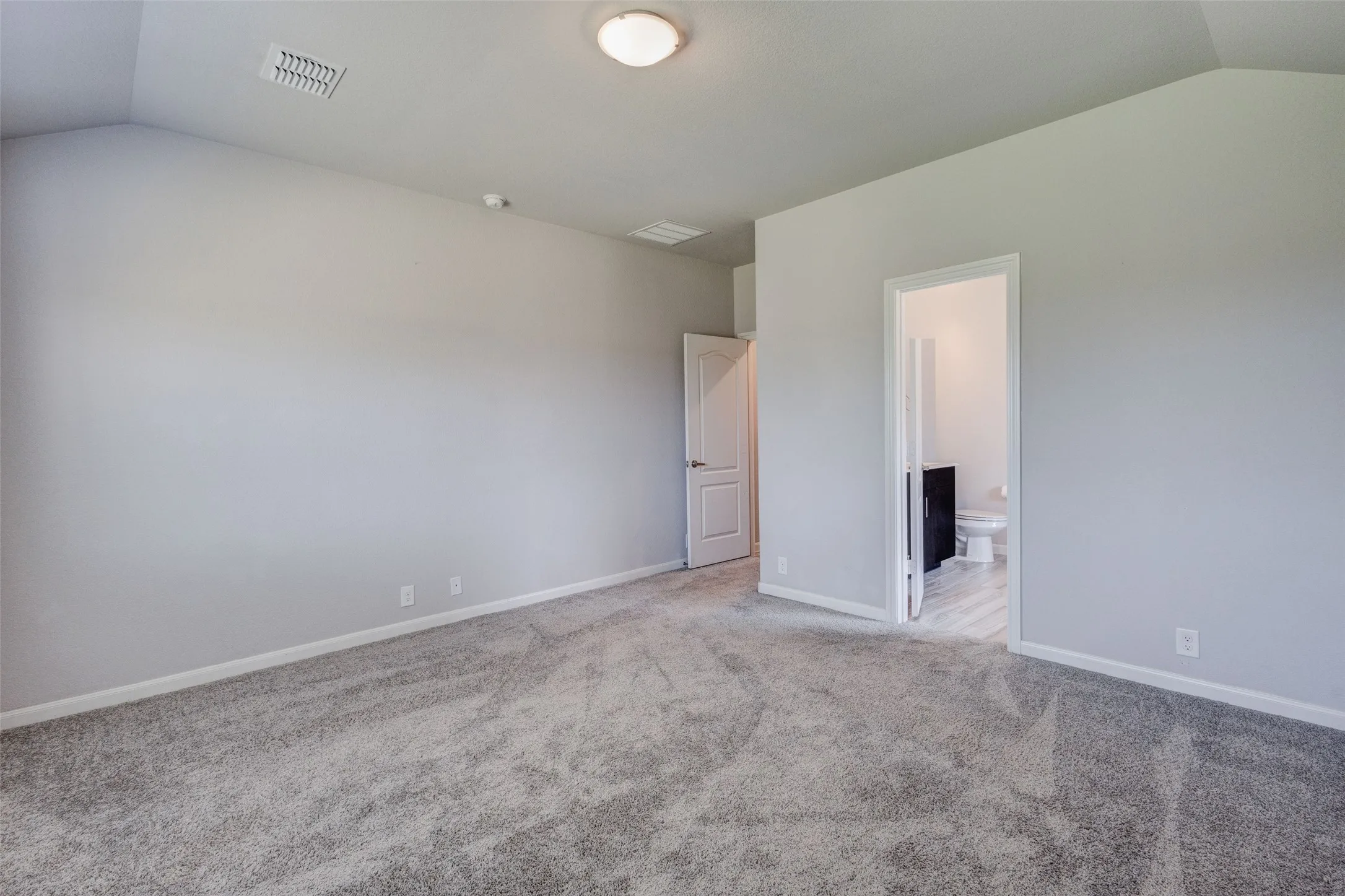 Spacious room featuring vaulted ceilings, light gray wall paint, and gray carpeting