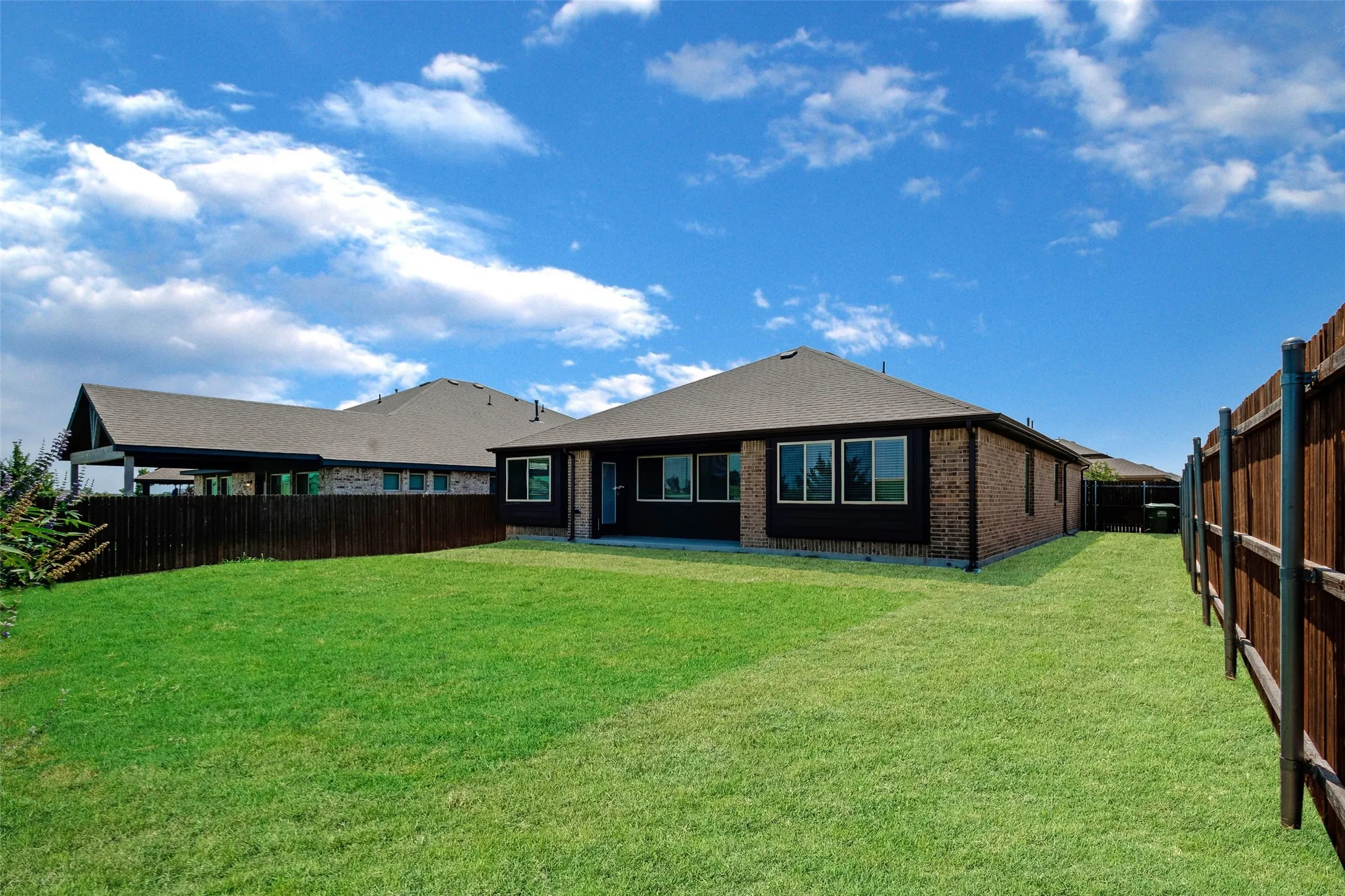 Expansive green lawn surrounds a brick residence with multiple windows and a covered patio
