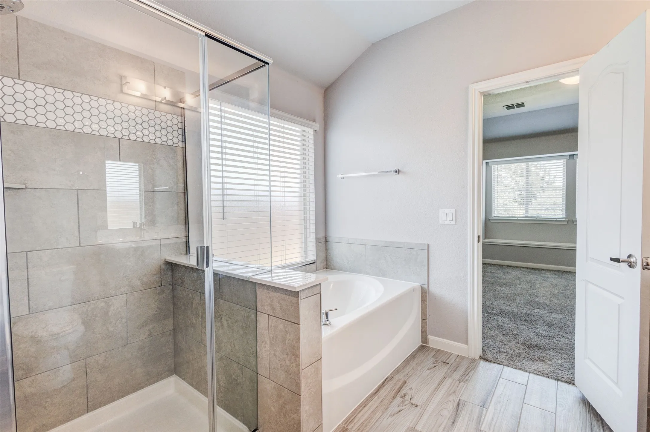 Bathroom featuring a glass-enclosed shower with tile surround, a built-in bathtub, and wood-finish flooring