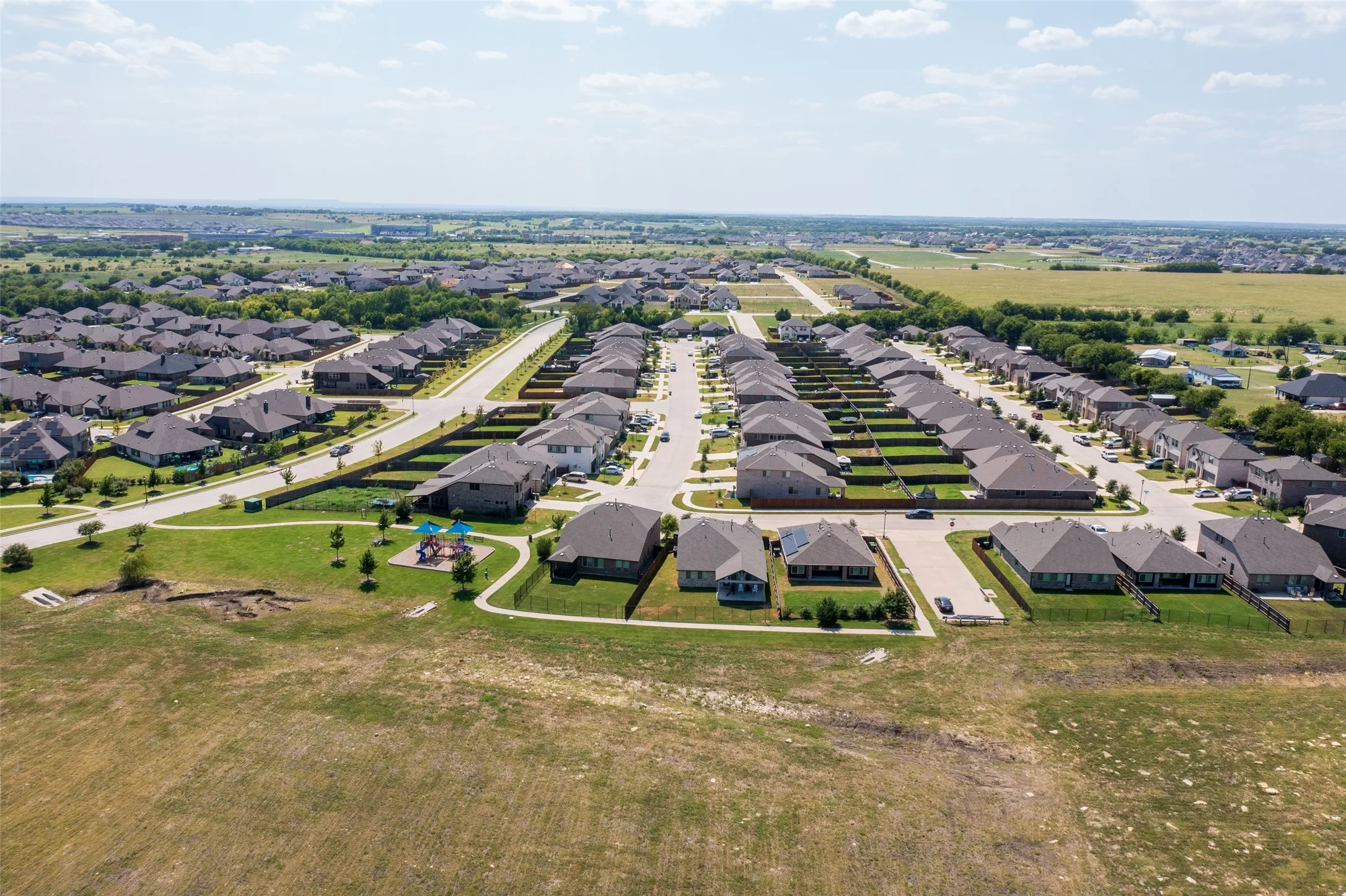 Aerial perspective of a developed residential area featuring numerous single-story homes with dark roofs