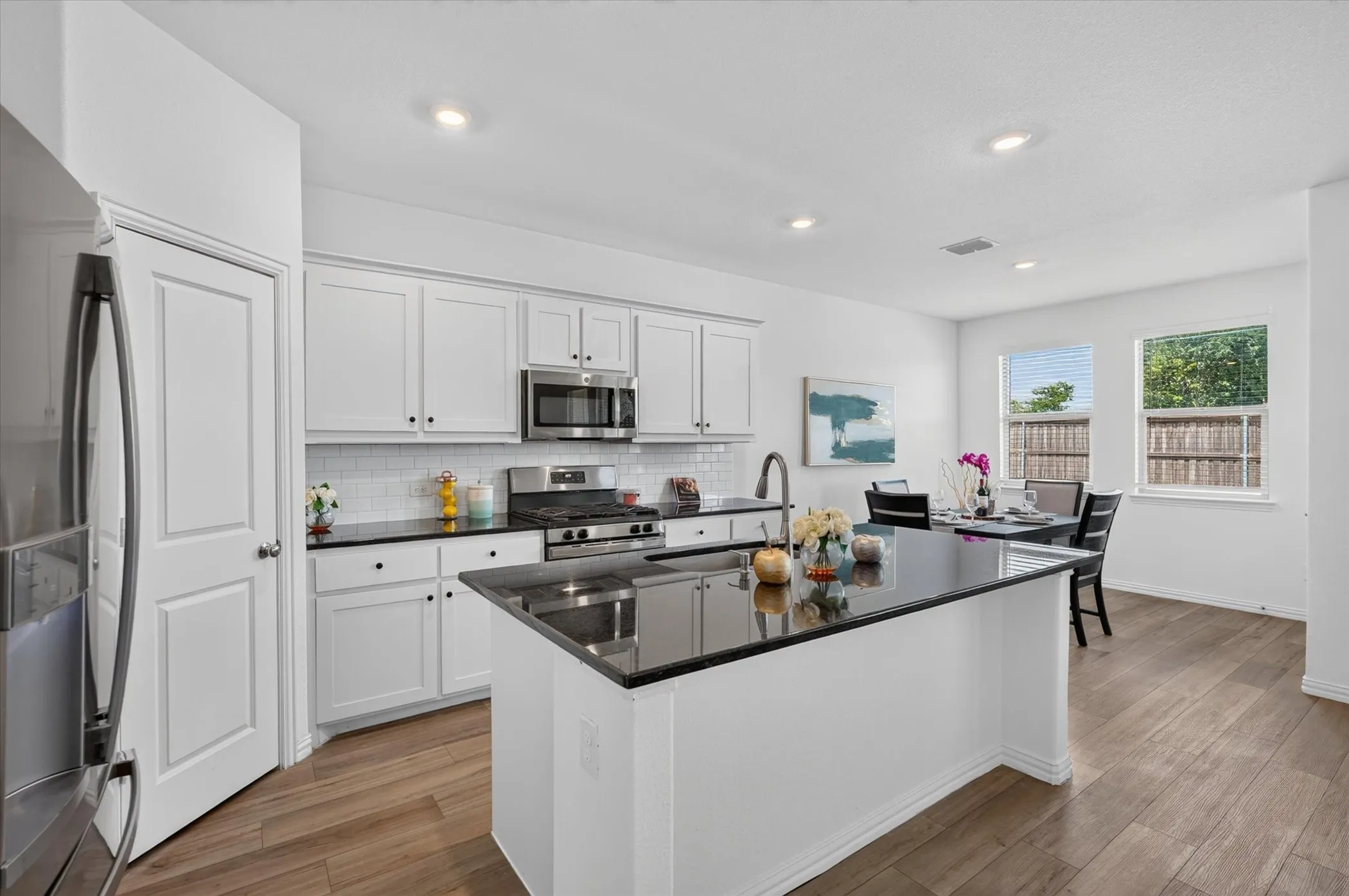 Bright kitchen featuring white cabinetry, dark countertops, white subway tile backsplash, stainless steel appliances, and wood-finish flooring