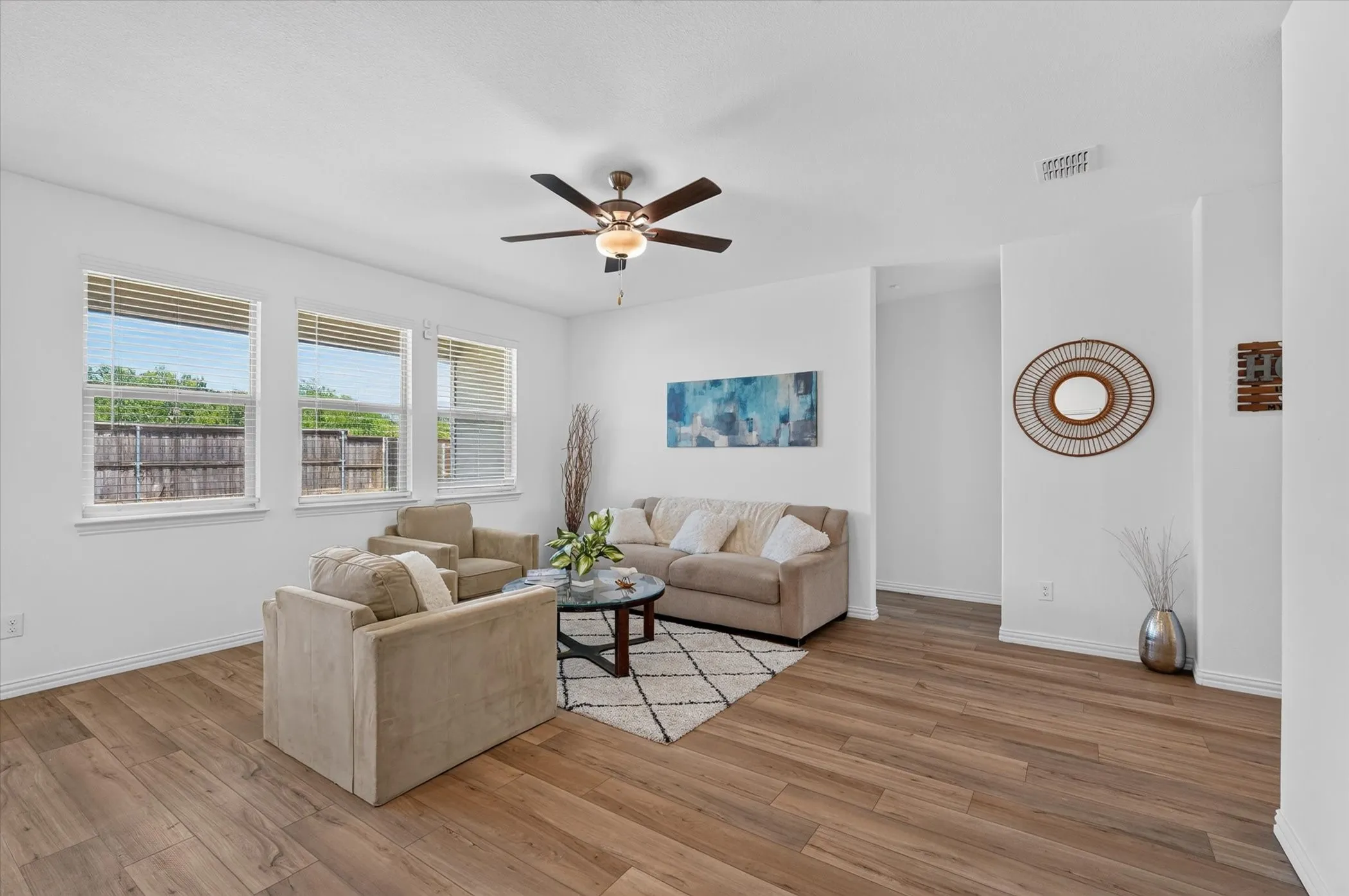 Spacious living area featuring wood-finish flooring, white walls, and a ceiling fan with integrated lighting