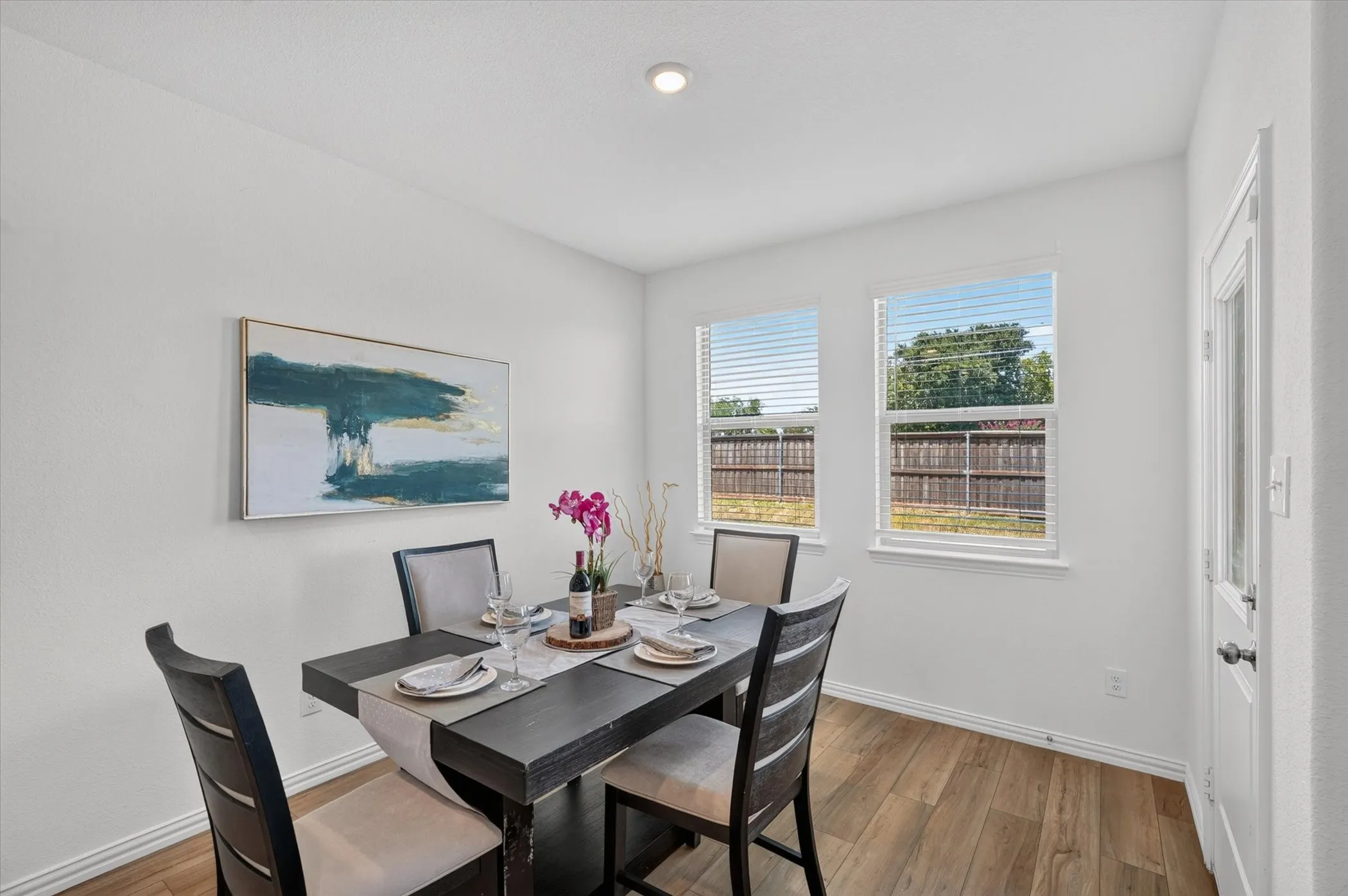Dedicated dining space featuring a black wood table with seating for four, wood-finish flooring, recessed ceiling lighting, and dual windows with plantation shutters offering natural light and outdoor views