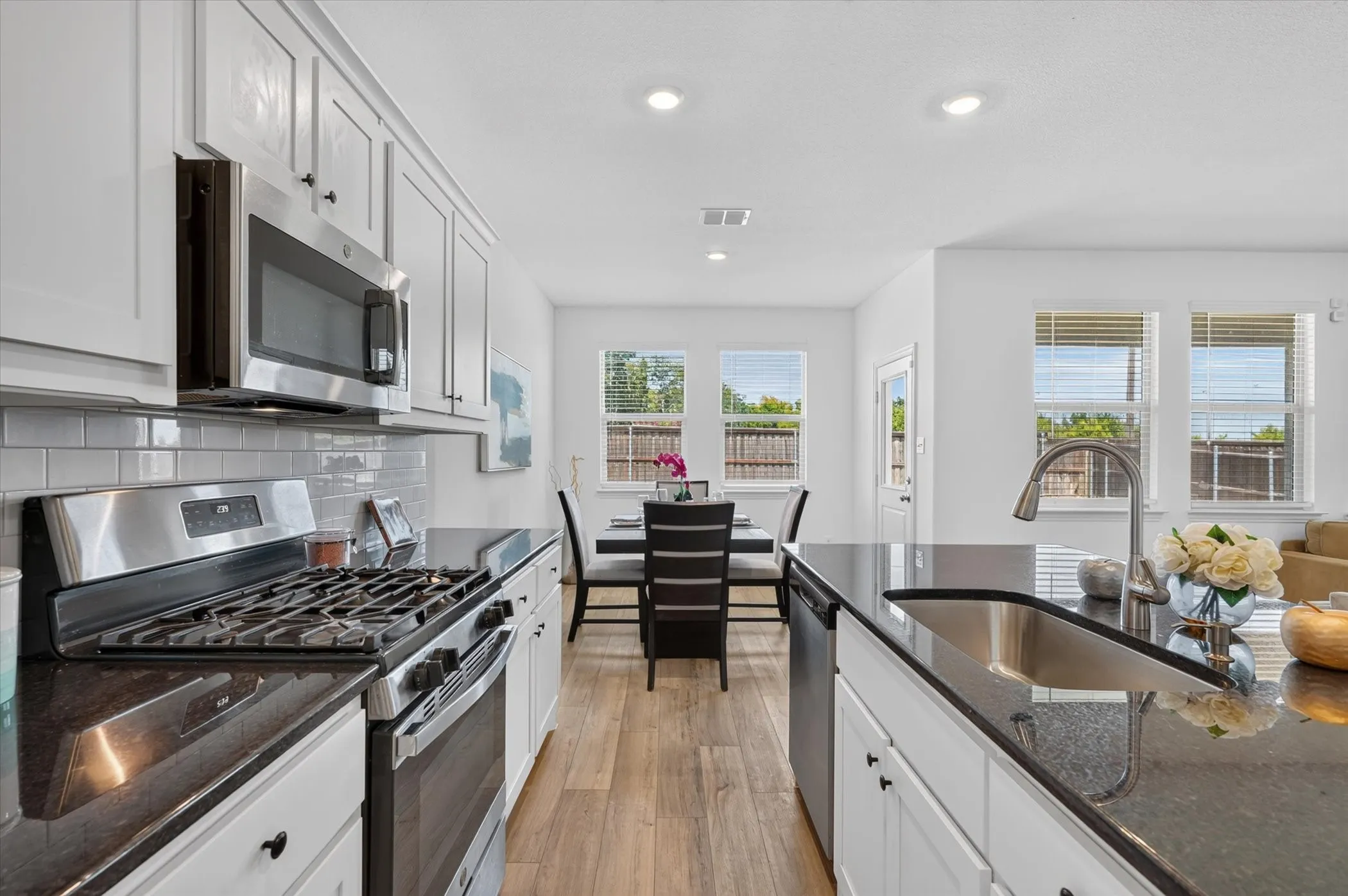 Chef's kitchen featuring white cabinetry, stainless steel appliances including a gas range and built-in microwave, dark quartz countertops, subway tile backsplash, and wood-finish flooring