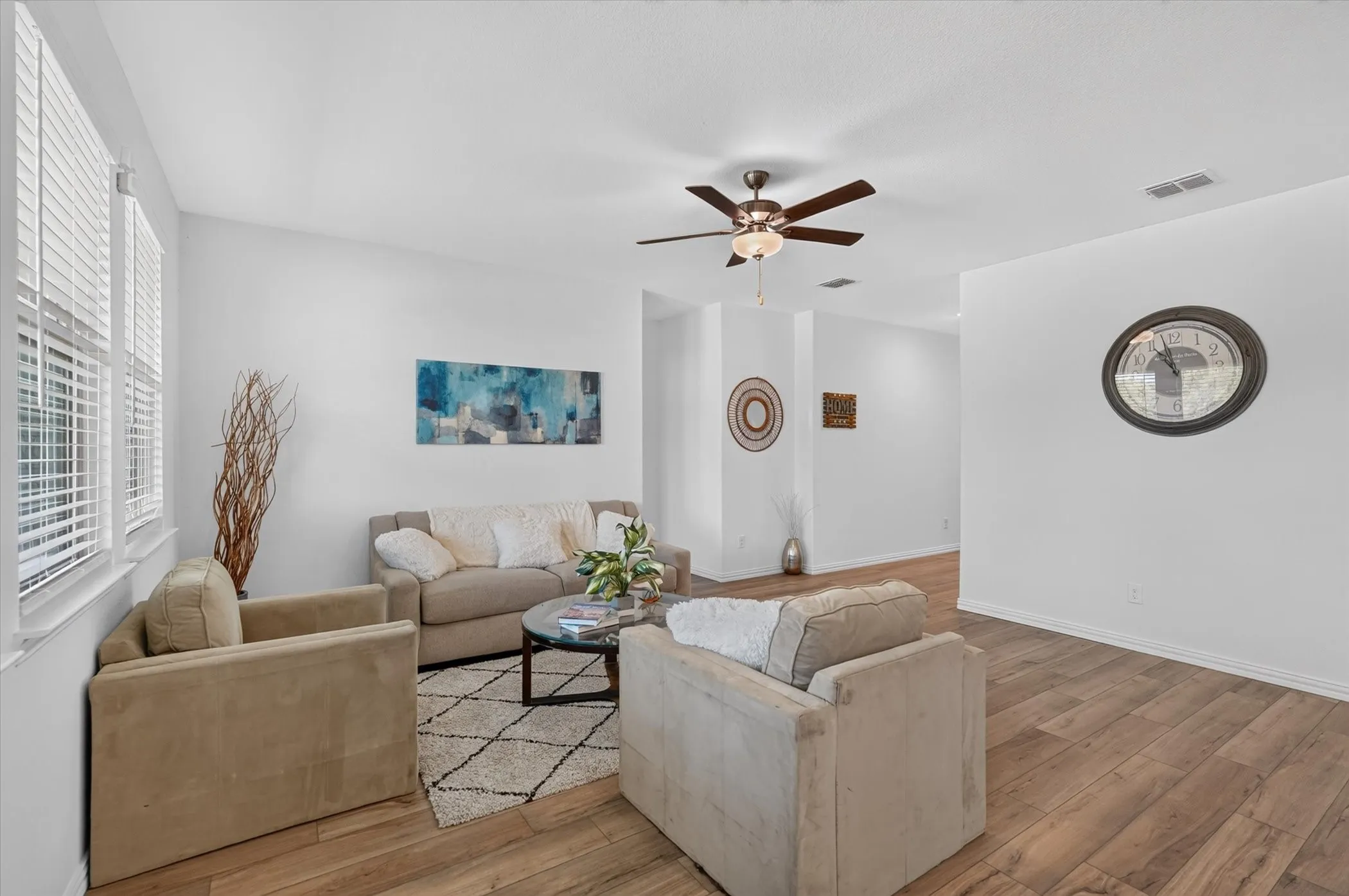 Living area featuring wood-finish flooring, white walls, and a ceiling fan with integrated lighting