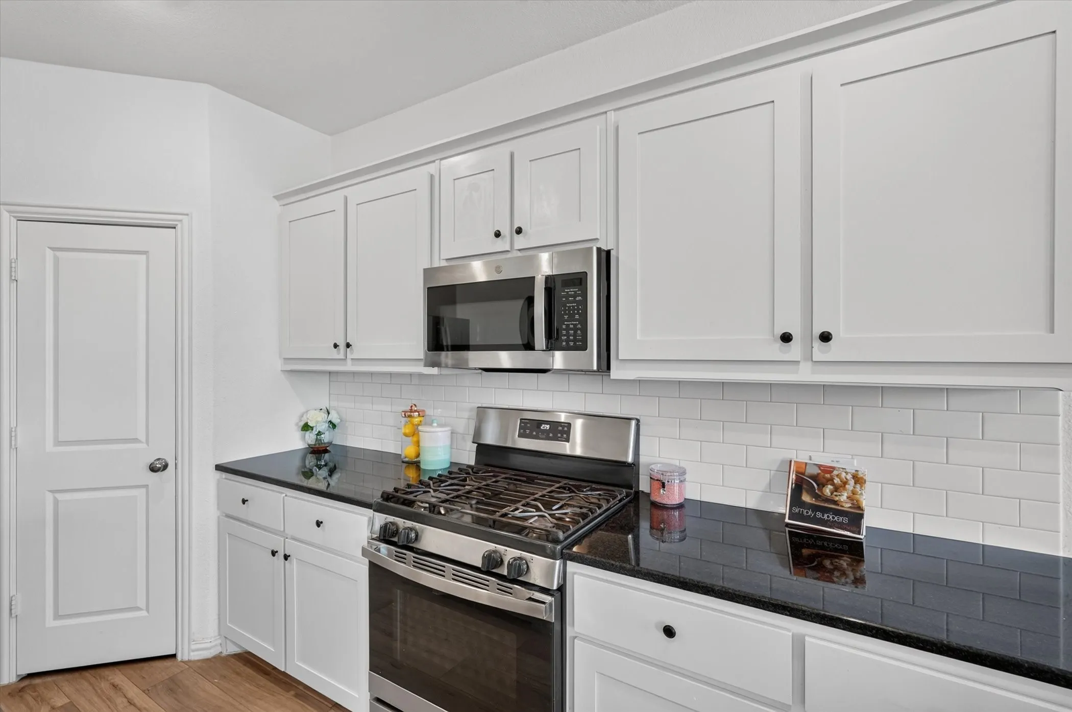 Kitchen featuring white shaker-style cabinetry, dark countertops, a stainless steel gas range, and a subway tile backsplash