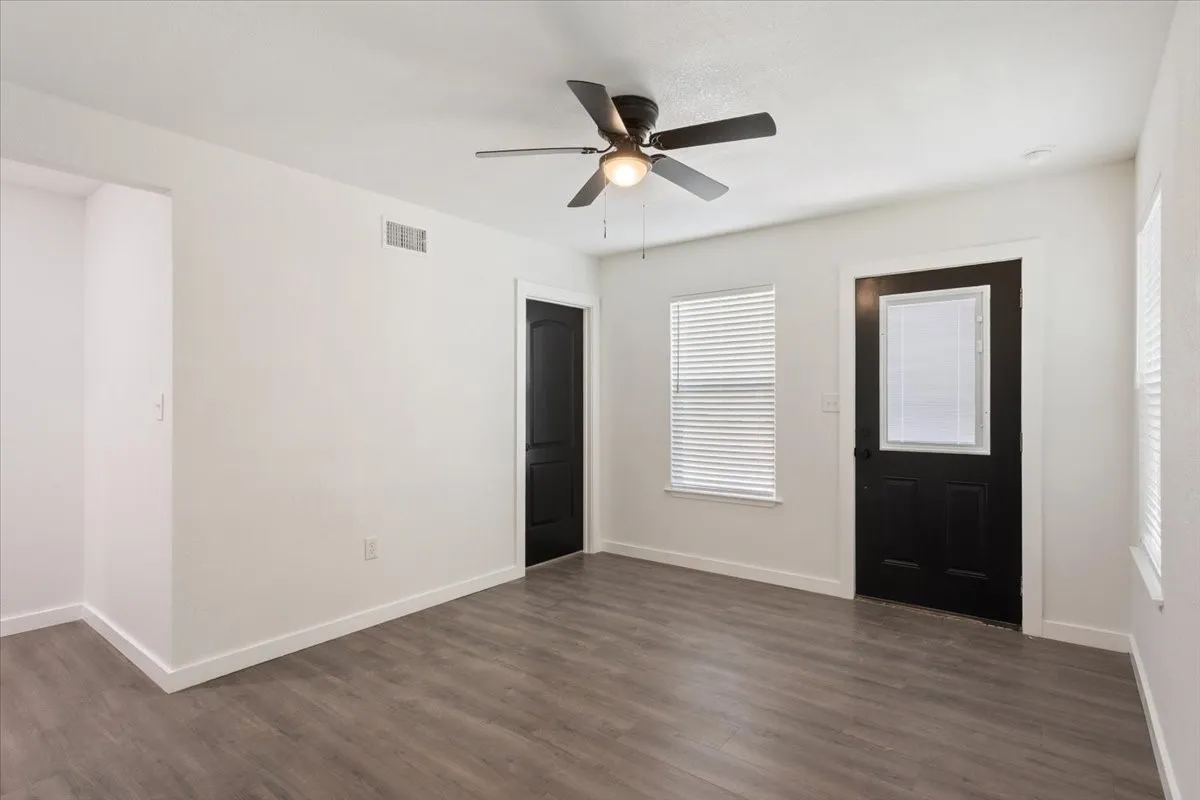 Living Room picture 1, by first primary bedroom, showing front door. Neutral-toned room featuring wood-finish flooring and bright white walls