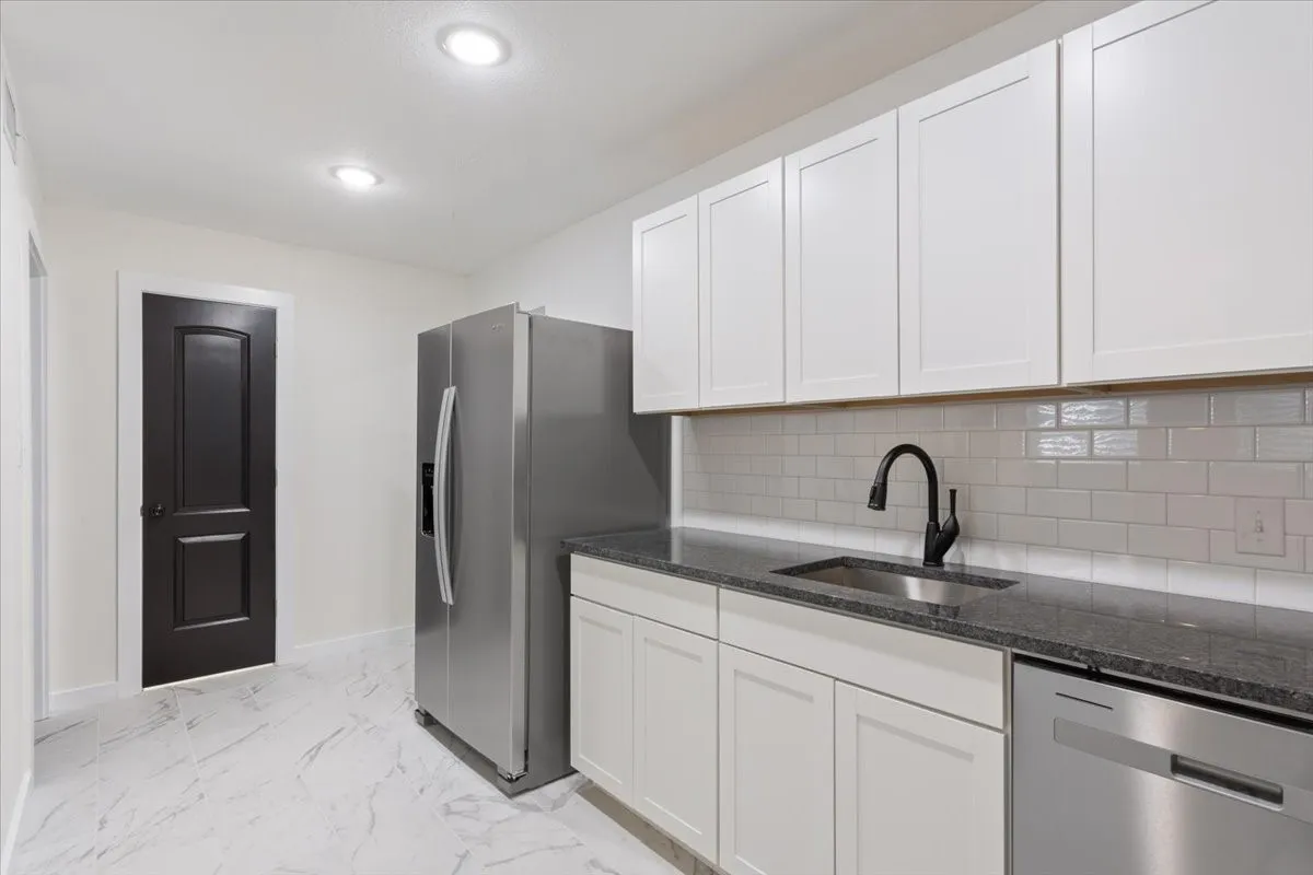 Modern kitchen featuring white shaker cabinetry, stainless steel appliances, dark stone countertops, and a subway tile backsplash. Showing door to Bathroom #2.
