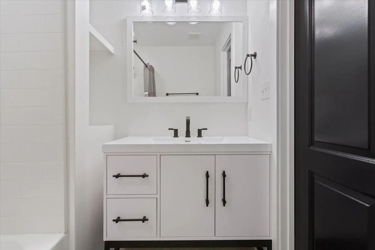 First primary bathroom #1. White vanity with black hardware, integrated sink, and wall-mounted faucet