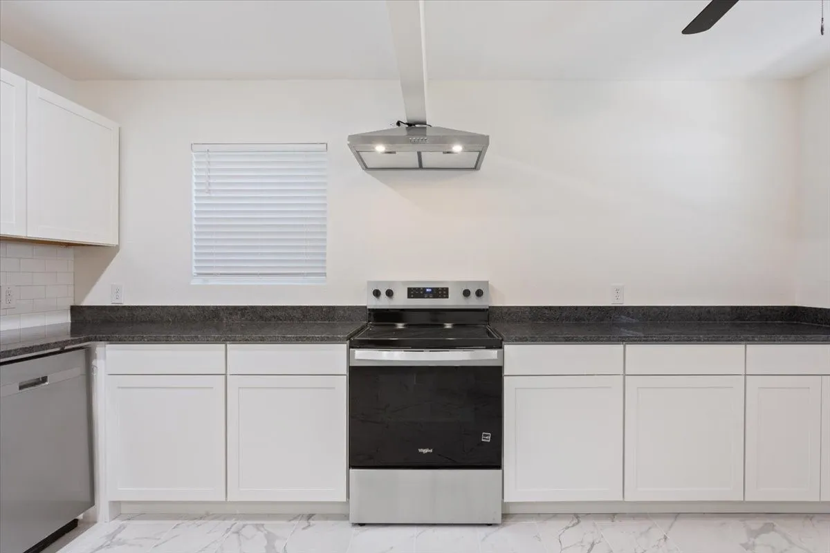 Contemporary kitchen featuring a stainless steel range with overhead hood, white shaker-style cabinetry, dark speckled countertops, and a white subway tile backsplash