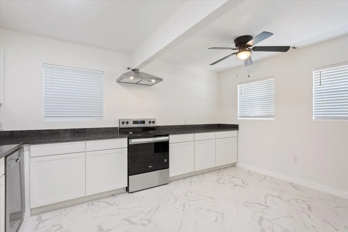 Kitchen featuring white cabinetry, dark countertops, a stainless steel range and range hood, and marble-look tile flooring