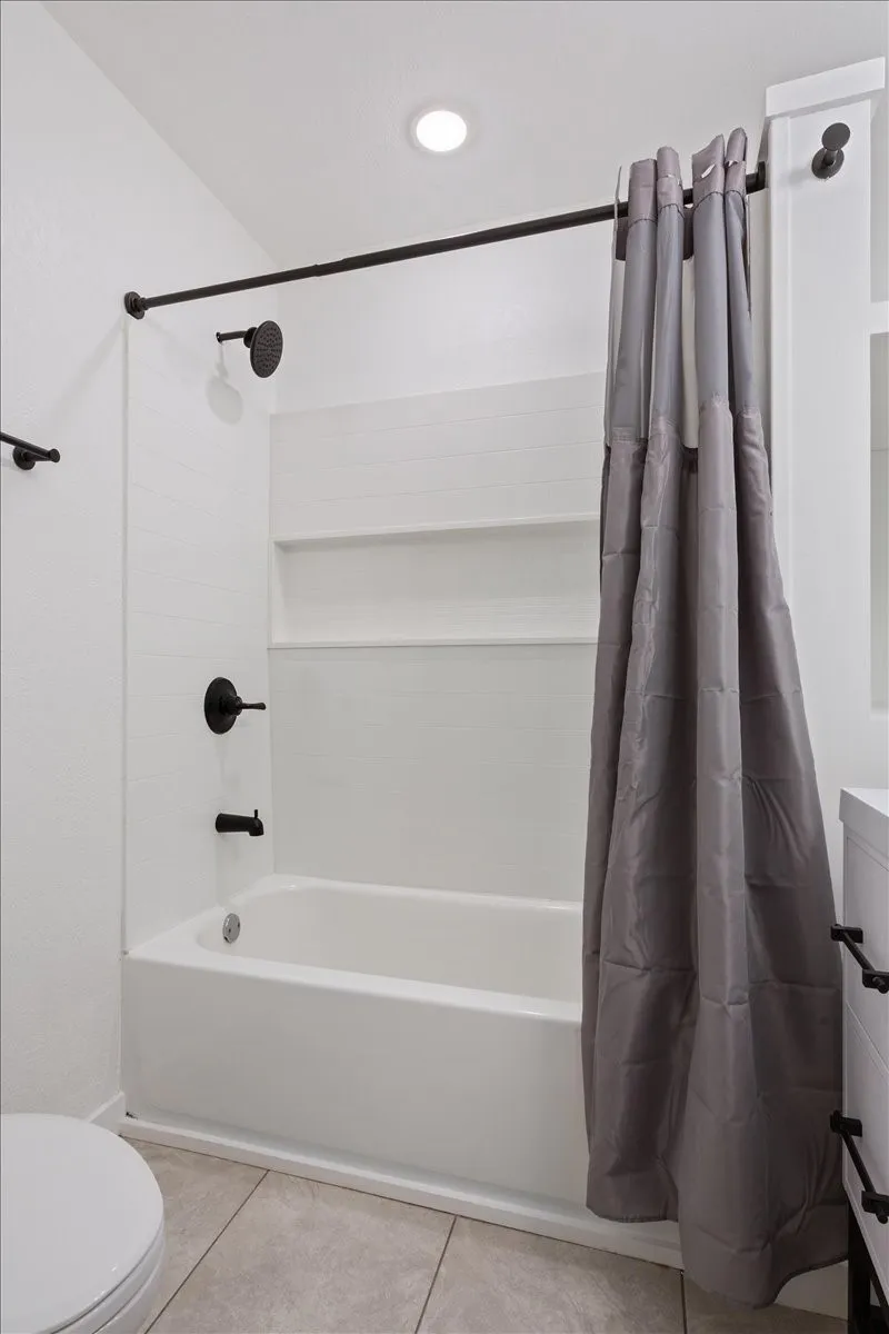 First primary bathroom #2. Bathtub and shower combination featuring a white surround with built-in shelving, matte black fixtures, and recessed lighting