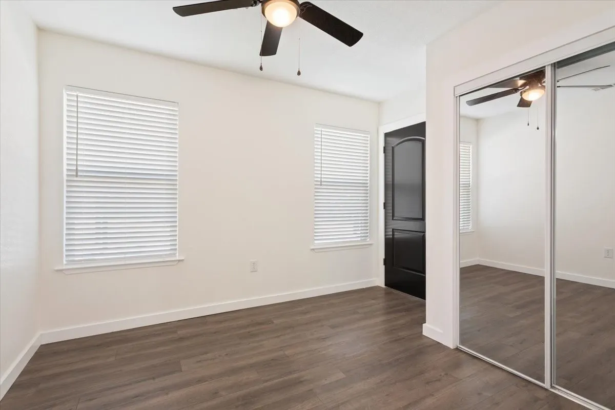First primary bedroom #2. Room featuring wood-finish flooring, two windows with blinds, a ceiling fan with integrated lighting, and a mirrored closet door
