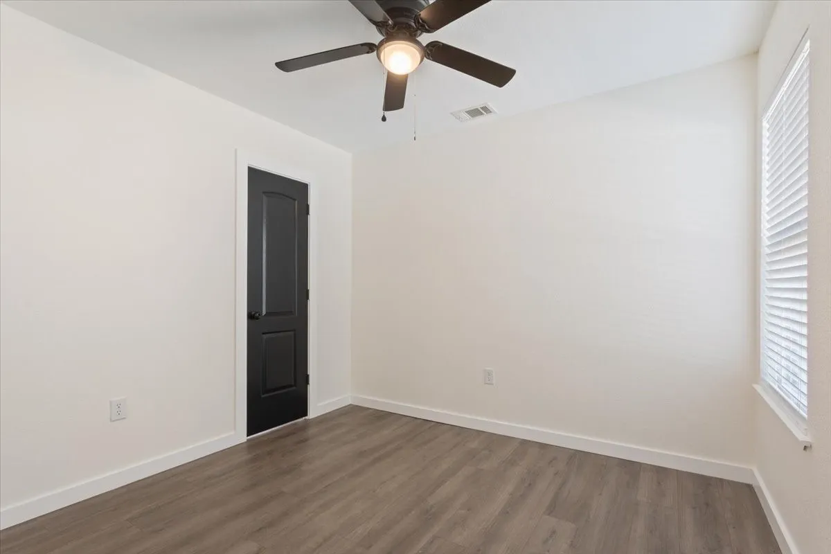 First primary bedroom #1. Room featuring wood-finish flooring, crisp white walls, and a contemporary dark-paneled door with white trim